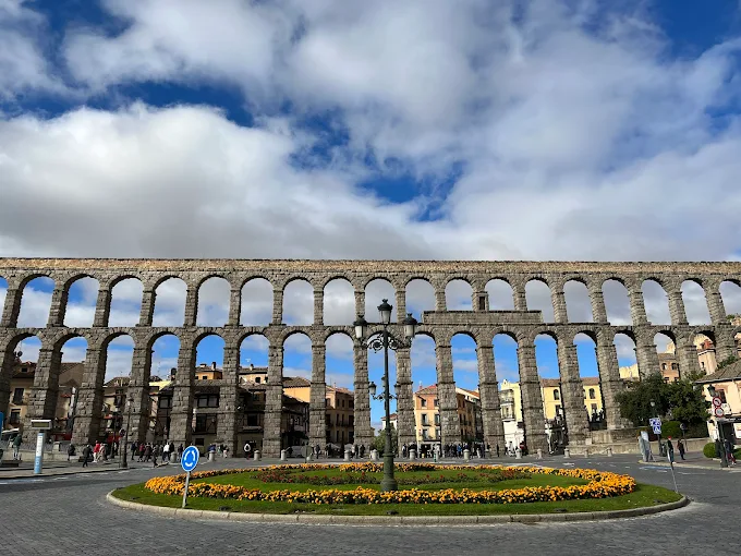 Segovia Aqueduct Roman granite arches at sunset with Plaza del Azoguejo and historic buildings bathed in golden Castilian light