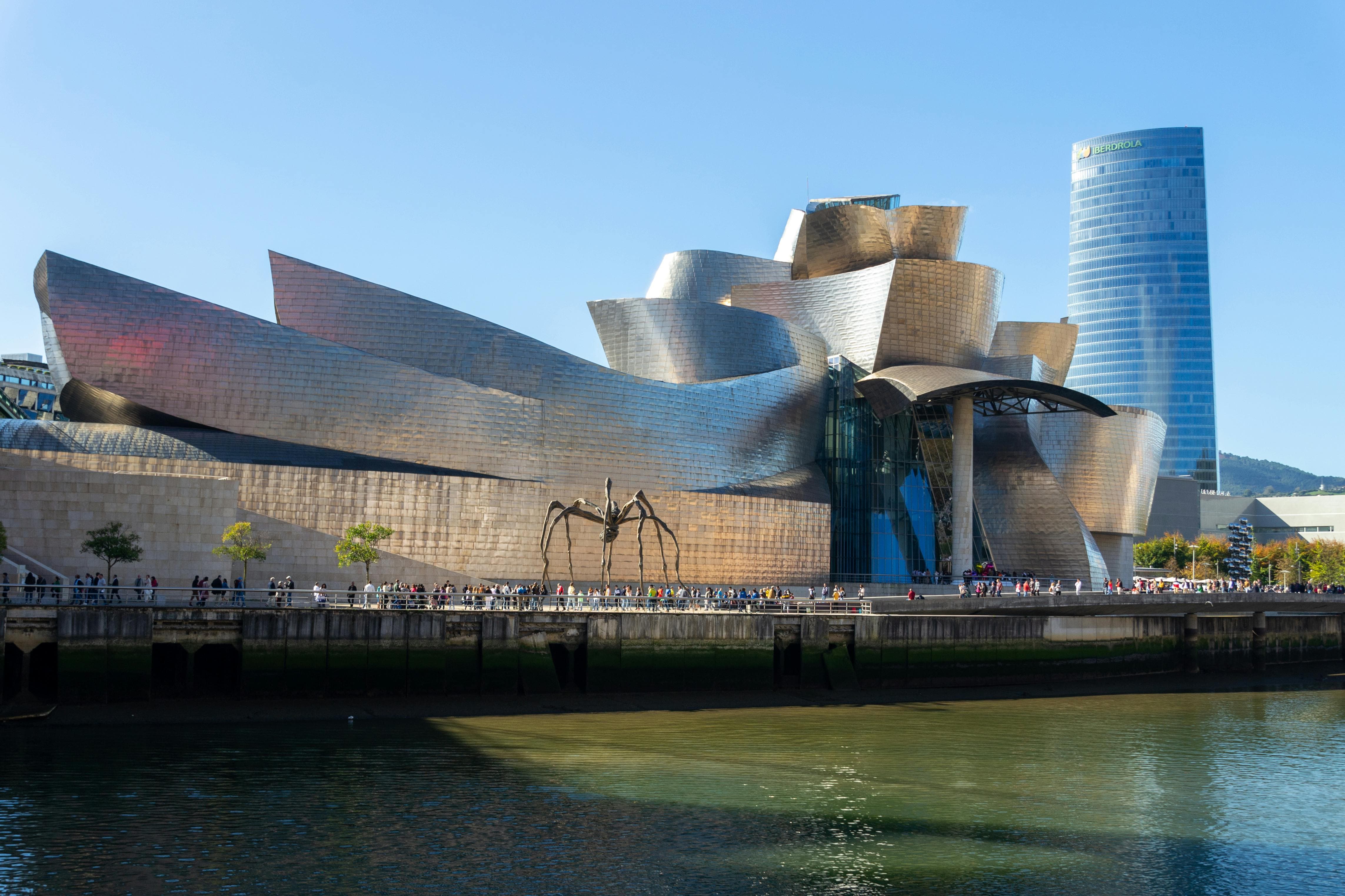 Guggenheim Museum Bilbao titanium curves reflecting on Nervión River at sunset in Basque Country, Spain with cloudy sky and modern architecture