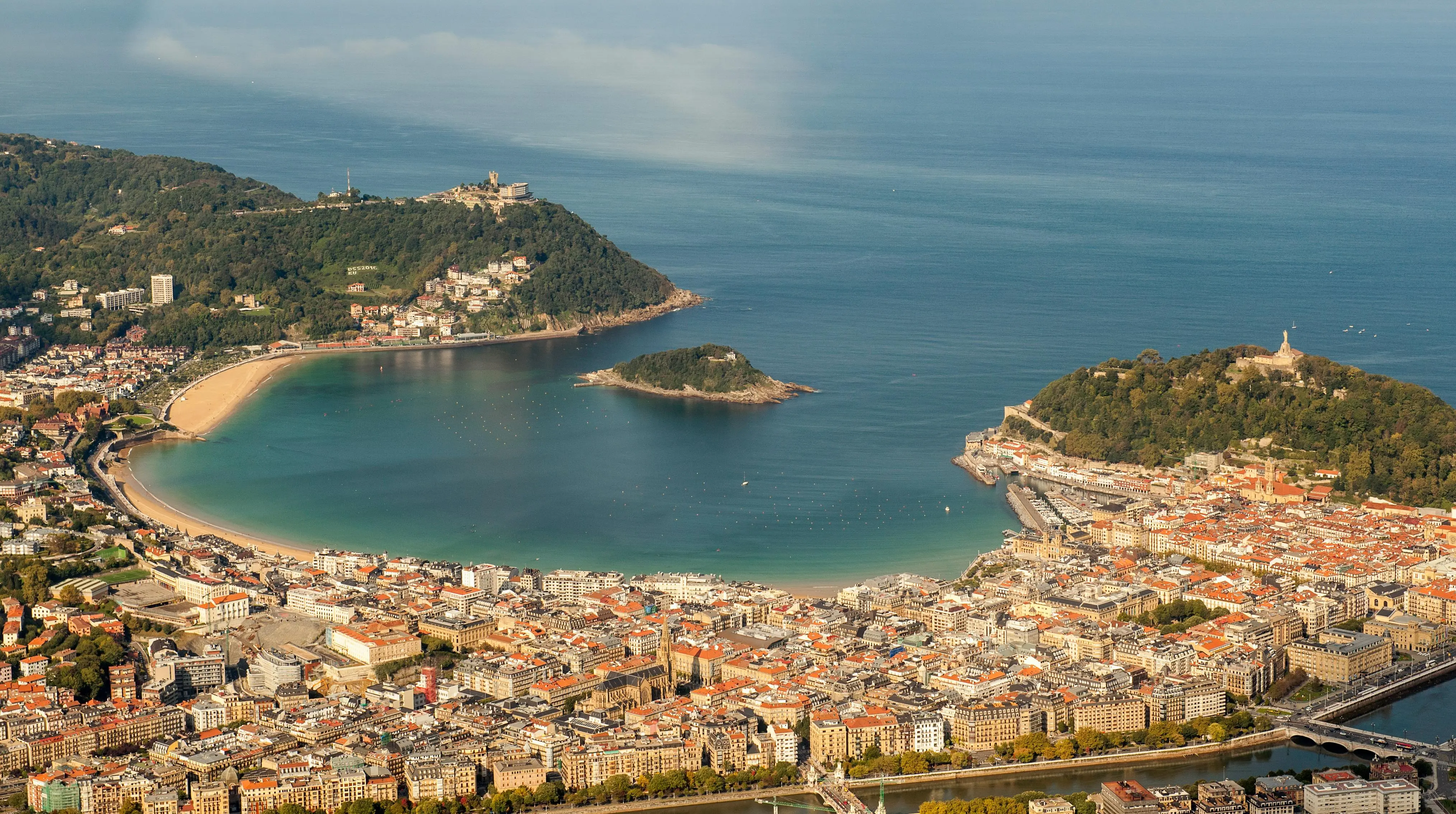 La Concha beach crescent bay with white sand and turquoise water at sunset in San Sebastián, Basque Country, Spain with city skyline