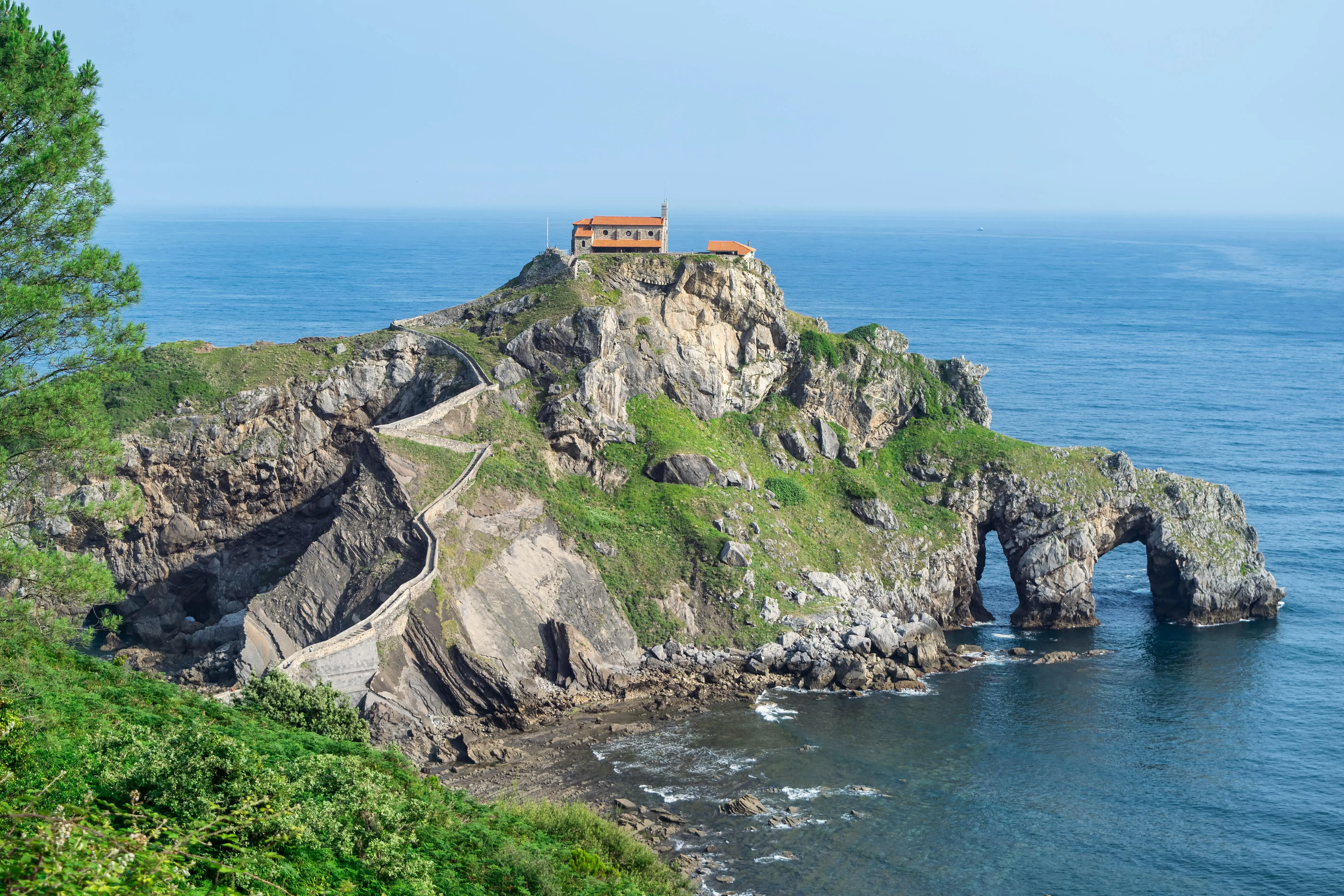 Gaztelugatxe island hermitage stone bridge and winding staircase rising from turquoise Bay of Biscay waters in Basque Country, Spain at morning light