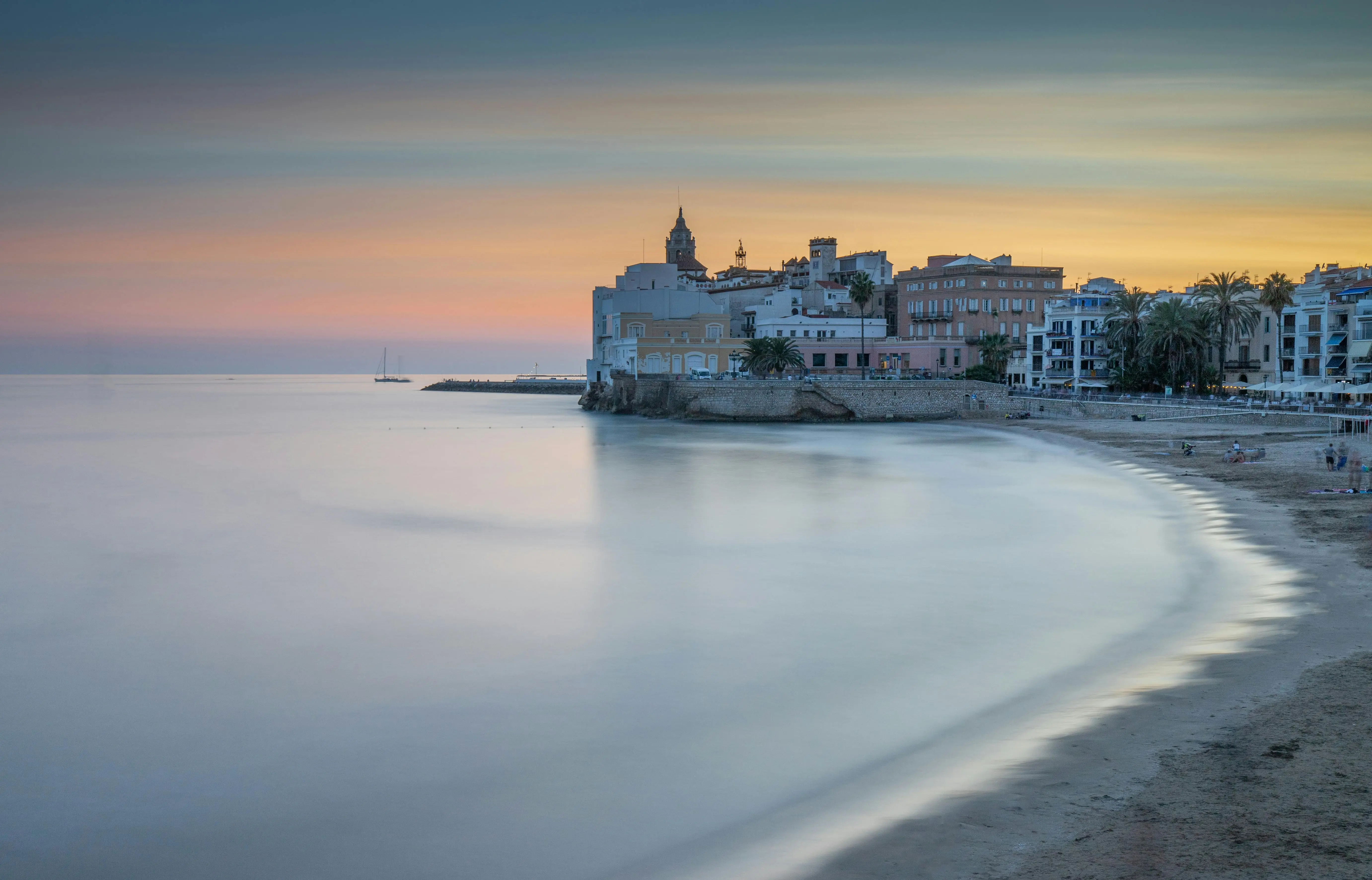 Sitges beaches golden sand at sunset with white church silhouette and Mediterranean sea, Catalonia coastal town, Spain