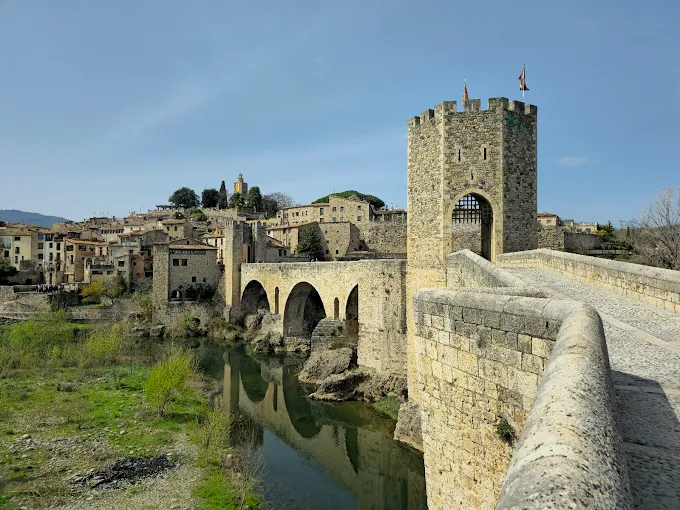 Besalú medieval bridge Pont Vell at sunrise with stone arches reflecting in Fluvià River, Catalonia, Spain