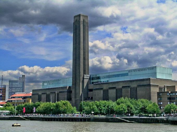 Tate Modern Turbine Hall at dusk with industrial brick facade and Thames River reflecting London skyline lights