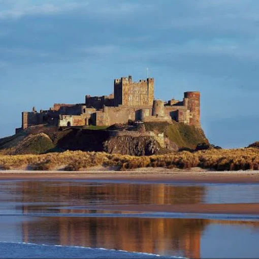 Bamburgh Castle medieval fortress at sunrise with volcanic rock, North Sea waves, and golden light in Northumberland