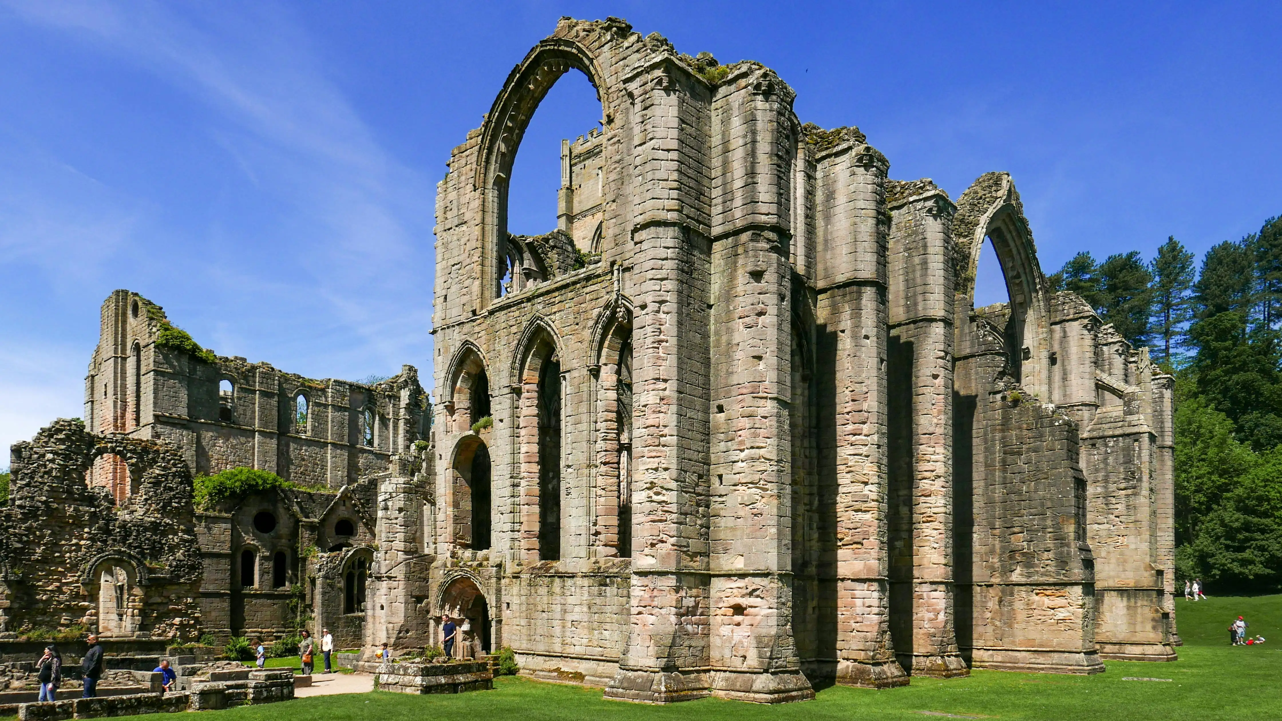 Fountains Abbey ruins at golden hour with stone arches, Skell River flowing, green lawns, and Ripon Valley background in North Yorkshire
