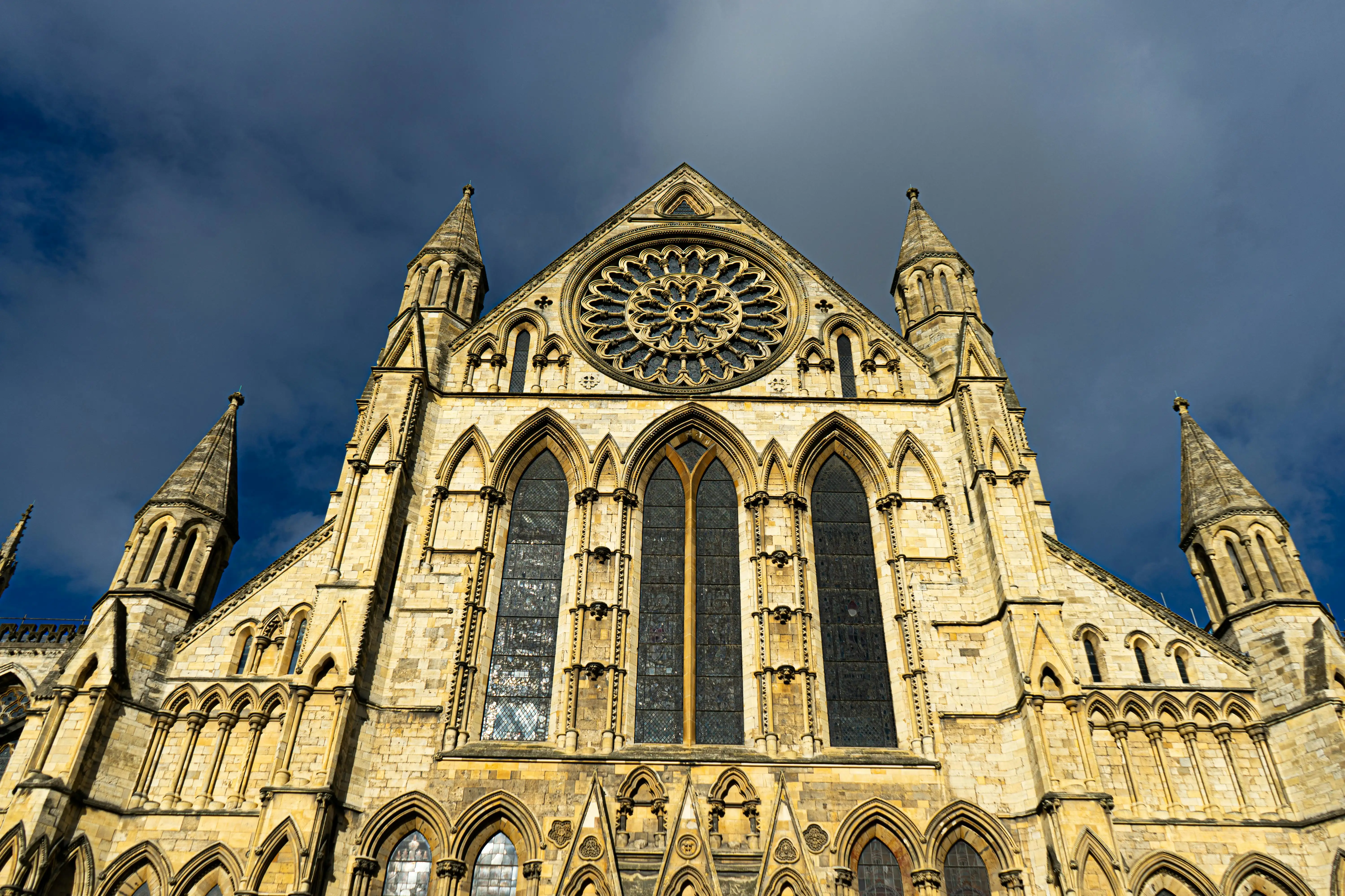 York Minster Gothic cathedral facade at sunset with stone towers, stained glass glowing, visitors walking on Minster Yard in York