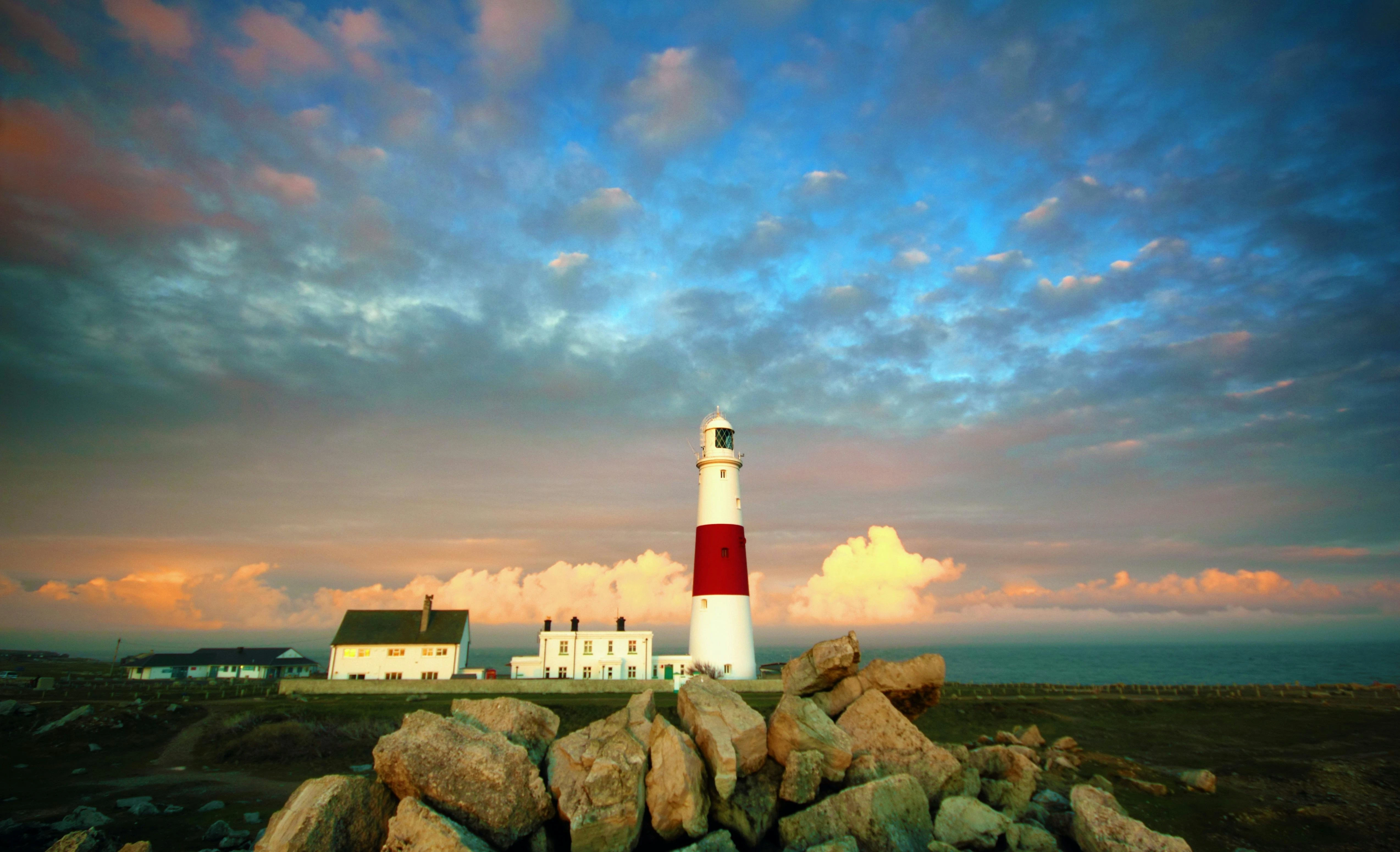 Portland Bill Lighthouse standing tall against stormy grey skies with white waves crashing on rocky Dorset coast England