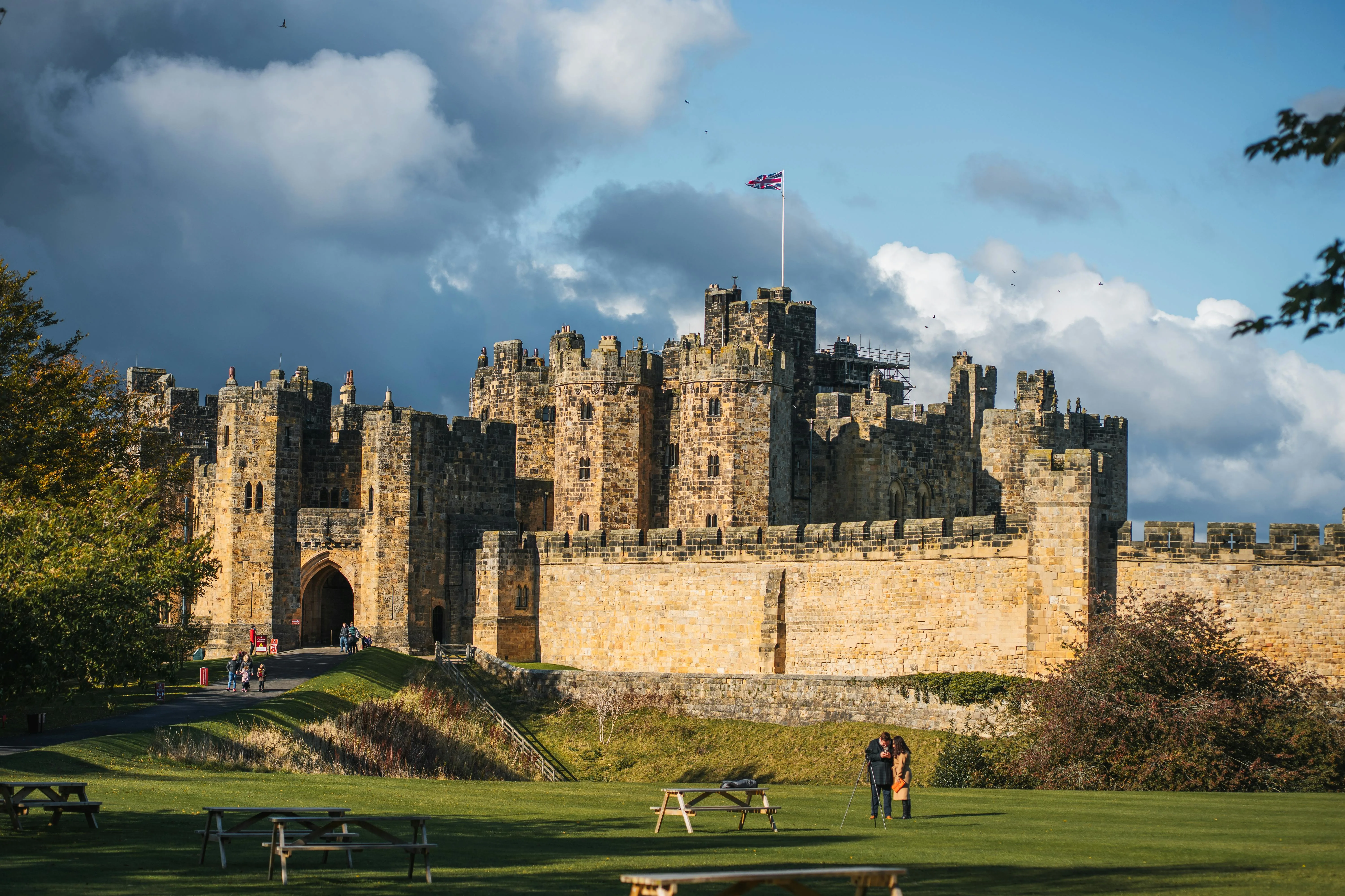 Alnwick Castle medieval fortress at sunrise with River Aln mist, stone towers, and Northumberland countryside background in England