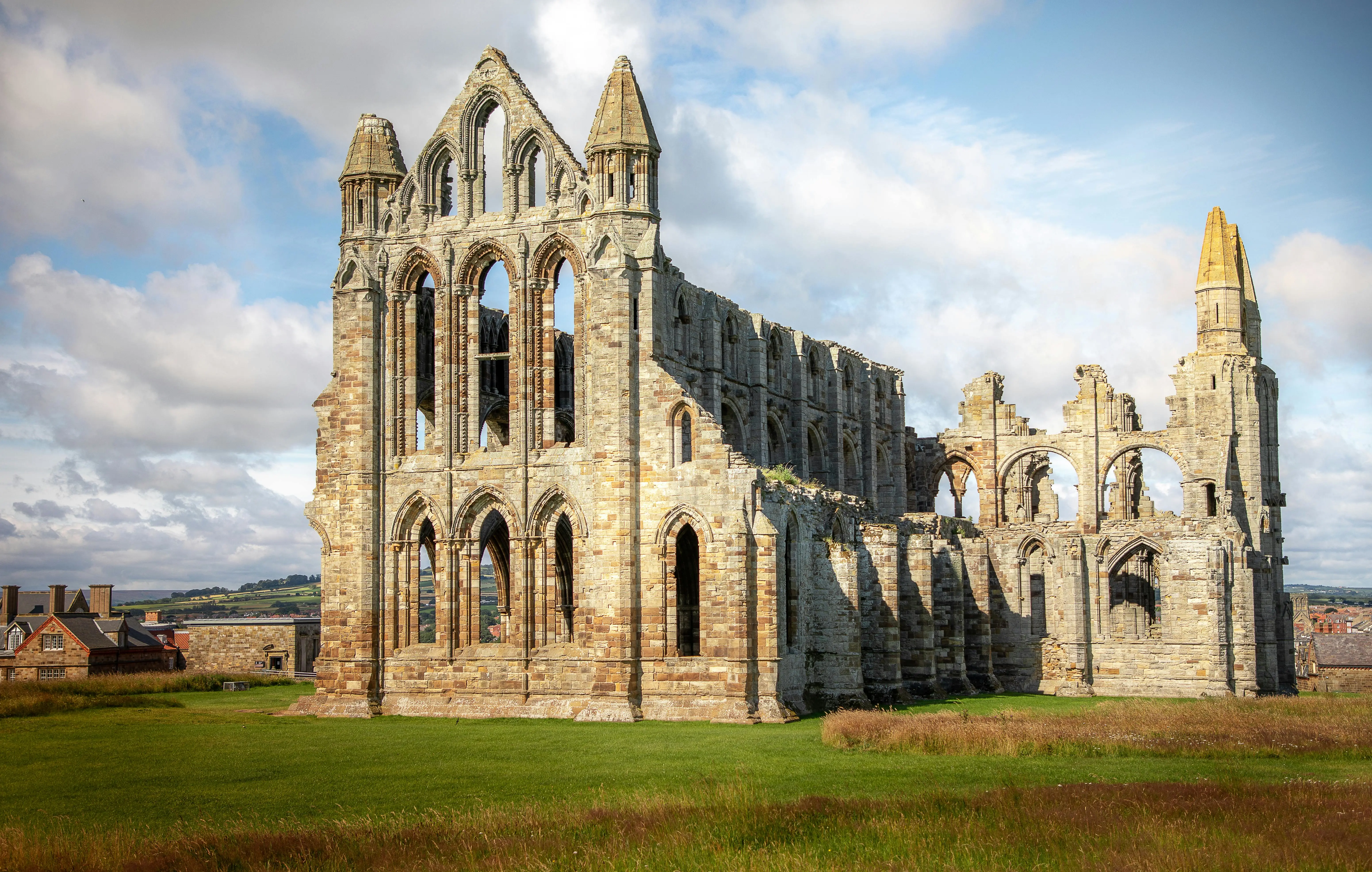 Gothic Whitby Abbey ruins on cliff edge at sunset with North Sea waves crashing below and seagulls flying overhead in North Yorkshire