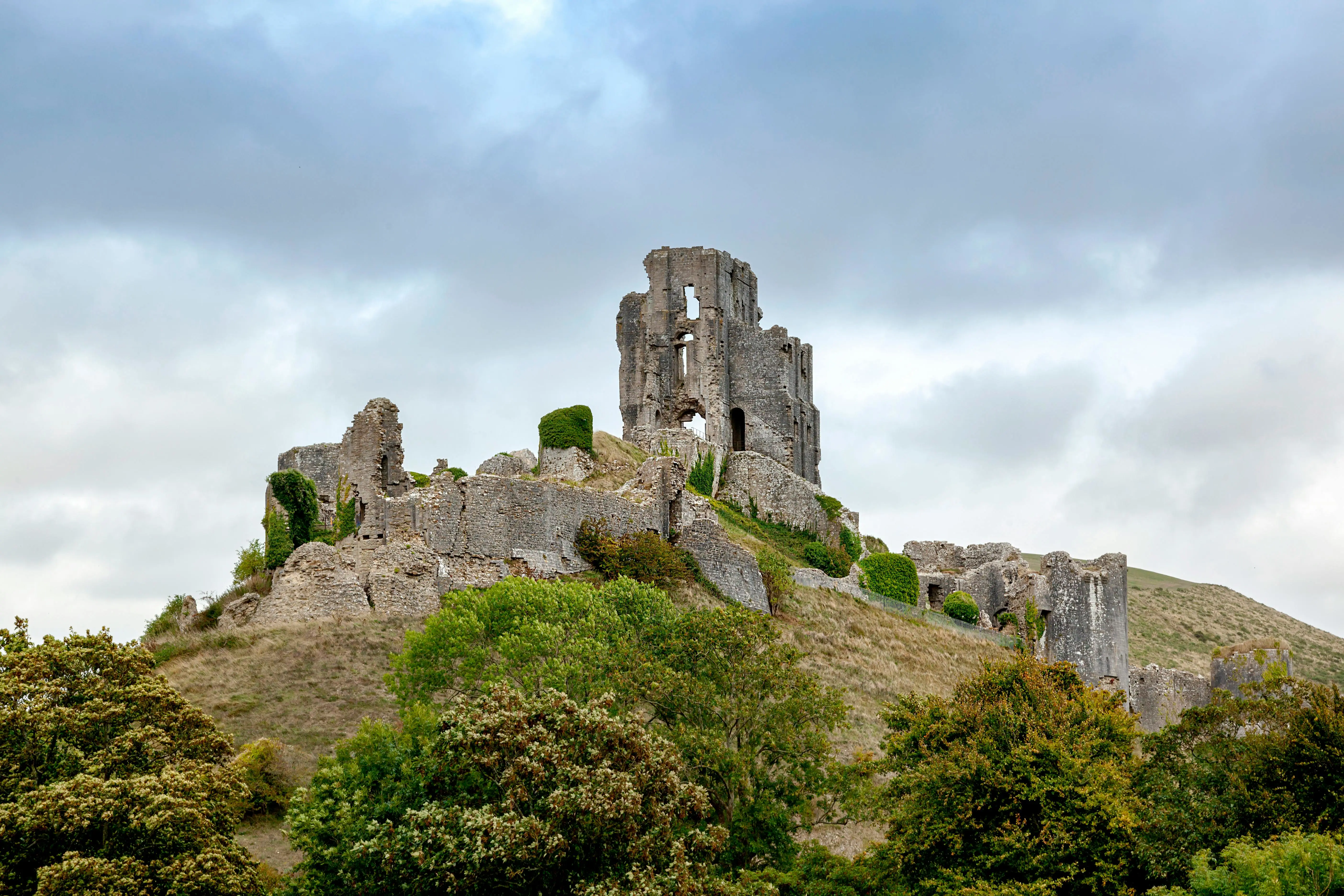 Corfe Castle ruins silhouetted against purple twilight sky with village lights glowing below in Dorset England