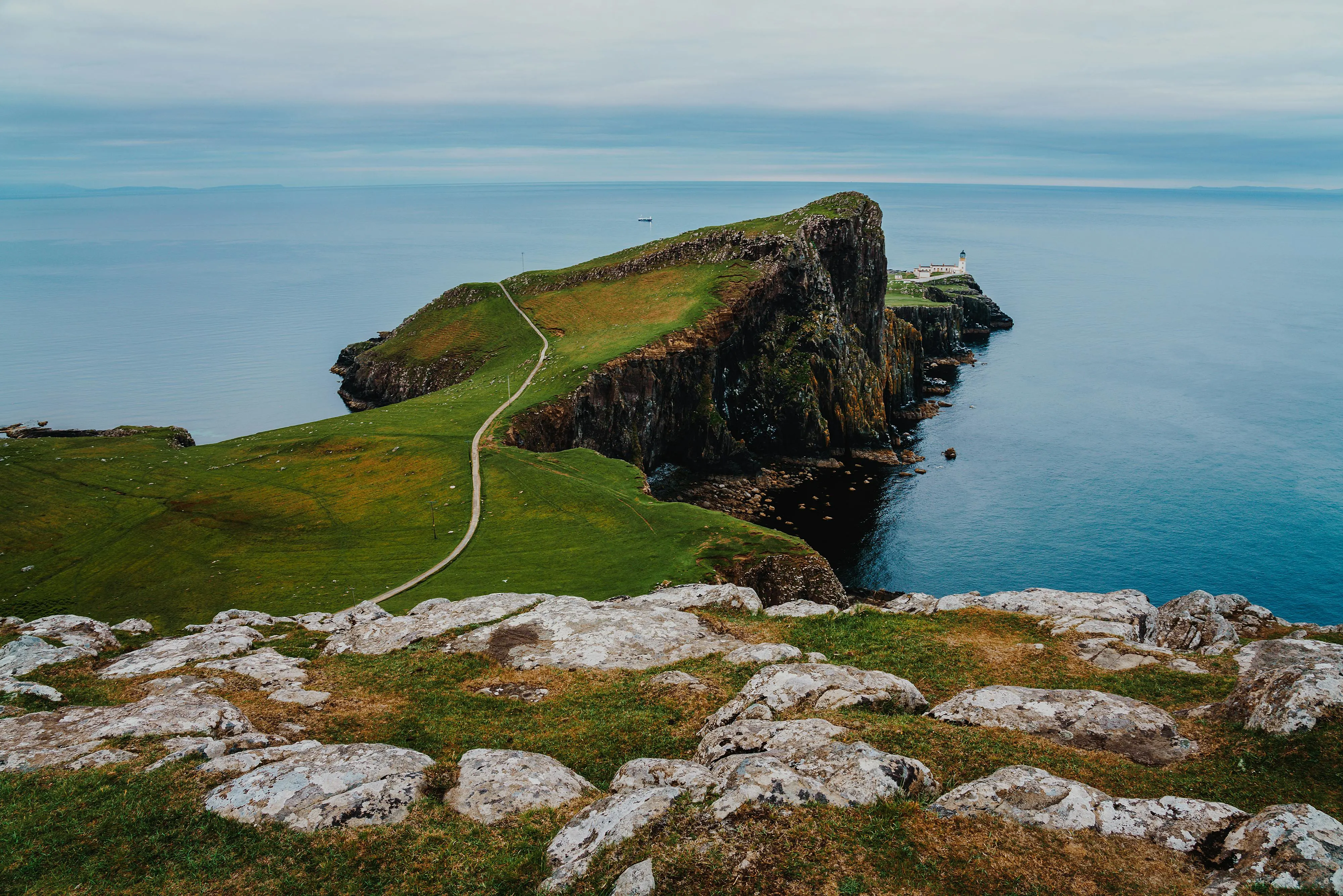 White Neist Point Lighthouse on dramatic cliff edge at sunset with crashing Atlantic waves and green grass in Isle of Skye Scotland