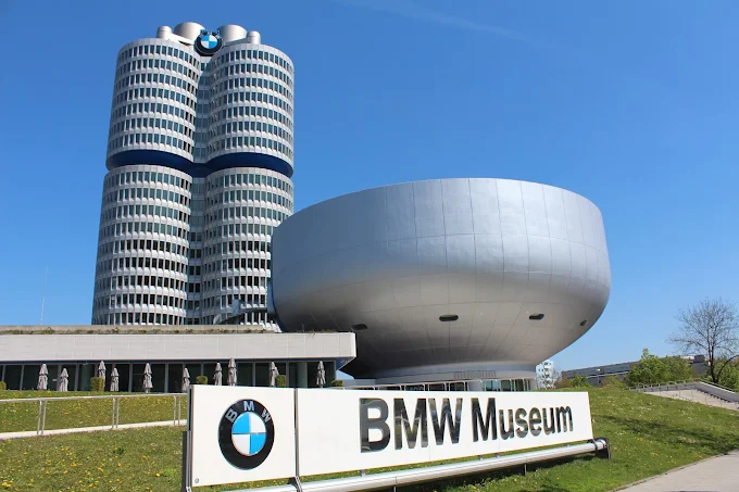 BMW Welt double cone architecture at sunrise with luxury cars on display, glass facade, and Munich skyline in Germany