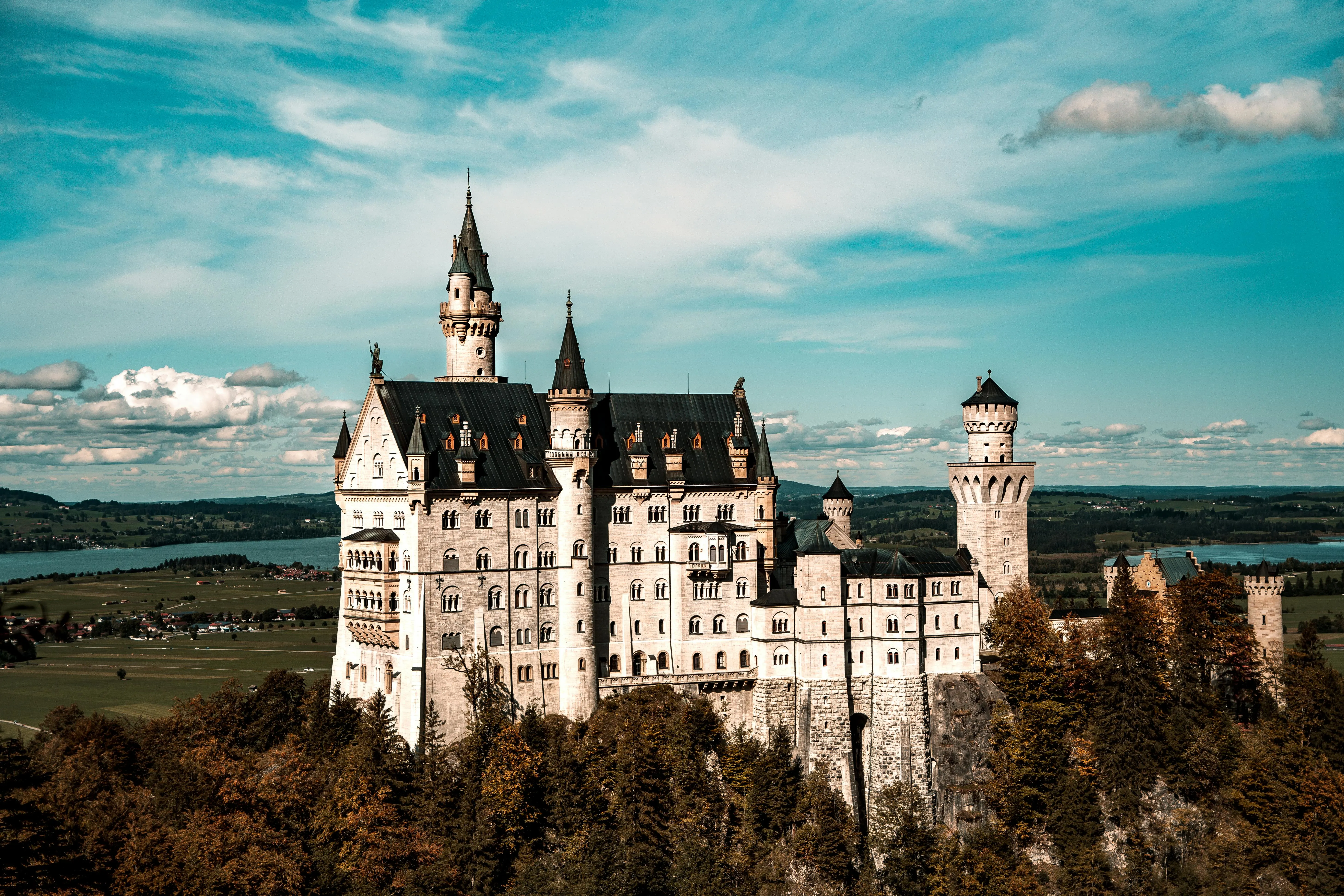 Neuschwanstein Castle white turrets at sunrise with Bavarian Alps backdrop, misty valley, and autumn foliage in Germany
