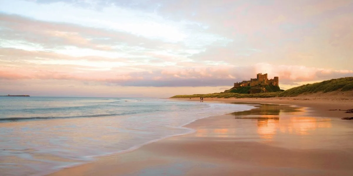 Northumberland beaches at sunrise with golden sand, Bamburgh Castle backdrop, and North Sea waves in England