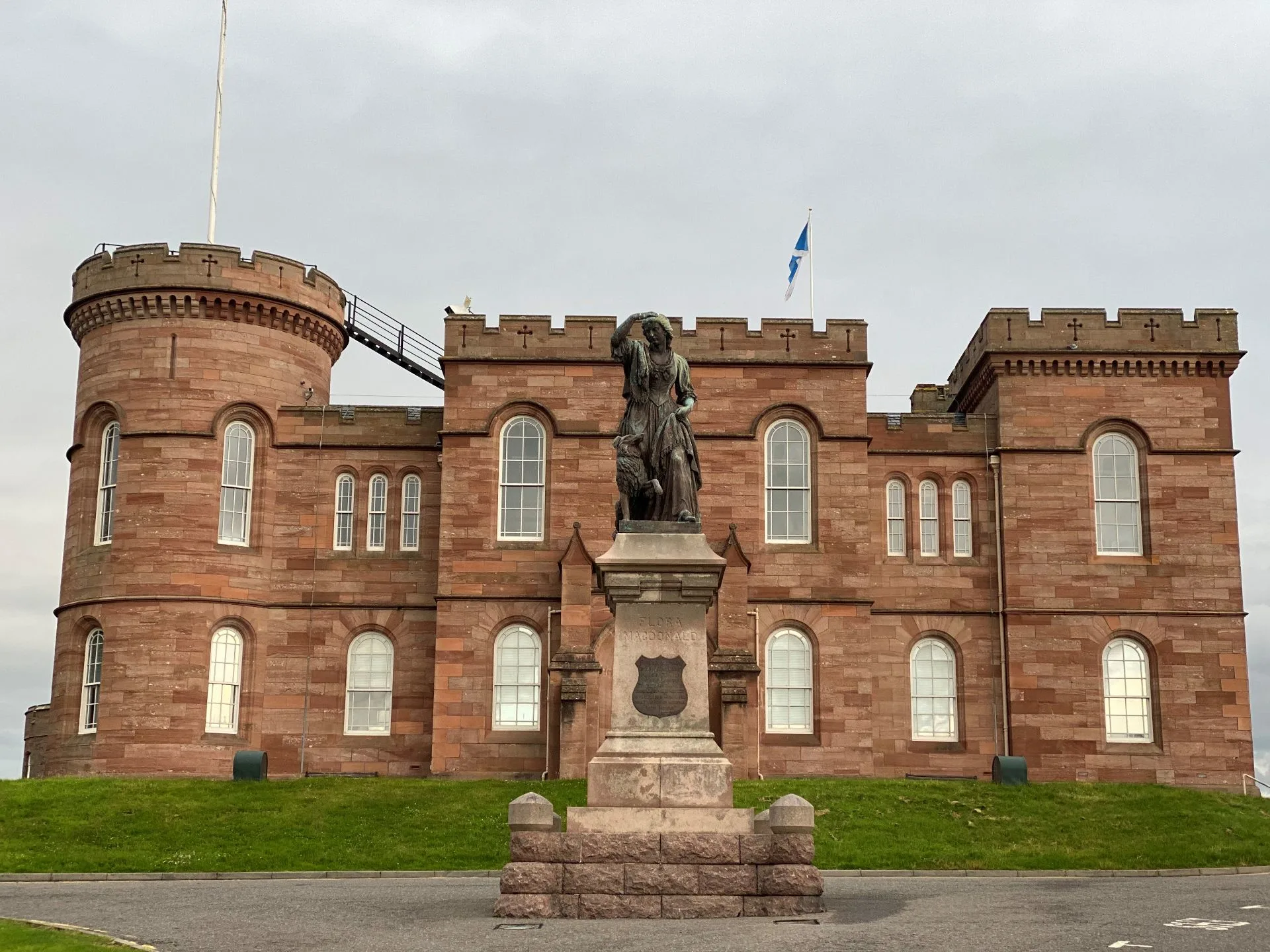 Inverness Castle red sandstone tower at sunrise overlooking River Ness with green banks and Scottish Highlands background