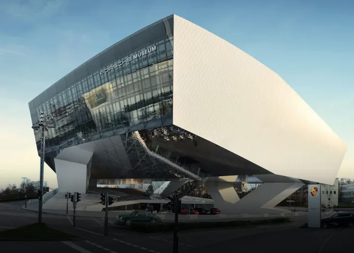 Porsche Museum white concrete architecture at sunset with silver sports cars, glass facade, and Stuttgart skyline in Germany