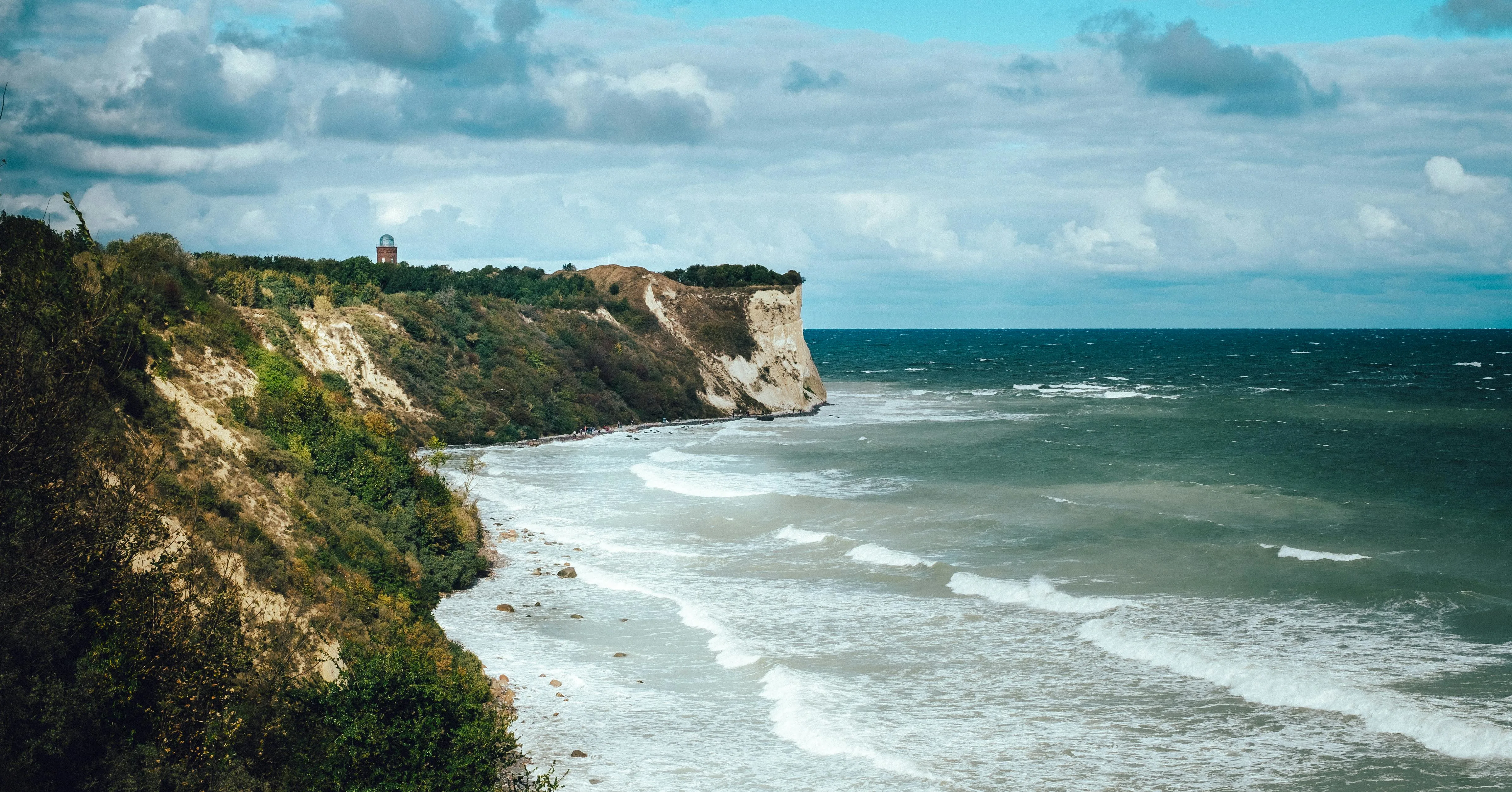 Rügen chalk cliffs at sunrise with white limestone faces, Baltic Sea waves, and green beech forest in Jasmund National Park Germany