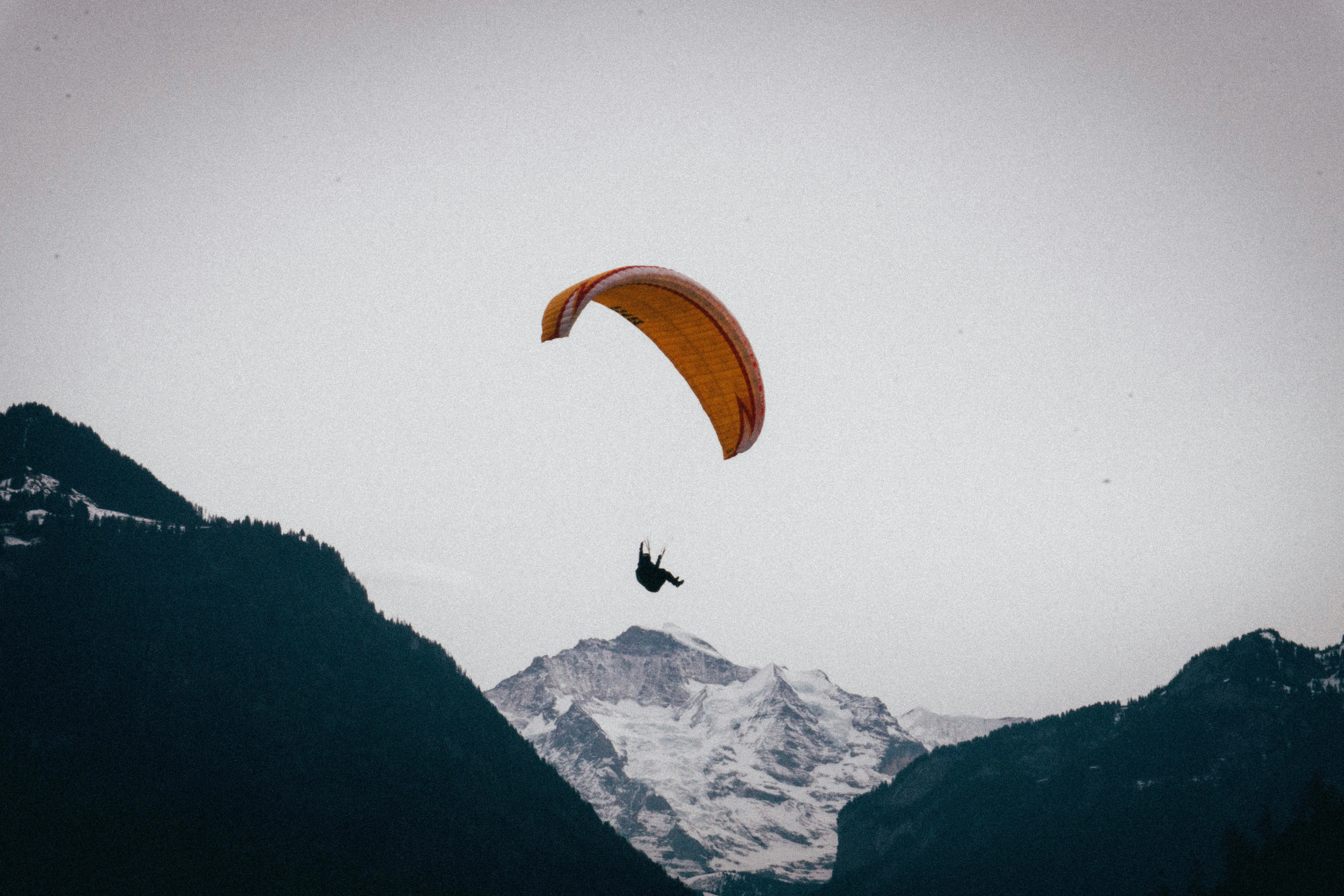 Interlaken adventure sports paraglider at sunrise with Jungfrau mountain, green valley, and blue sky in Switzerland