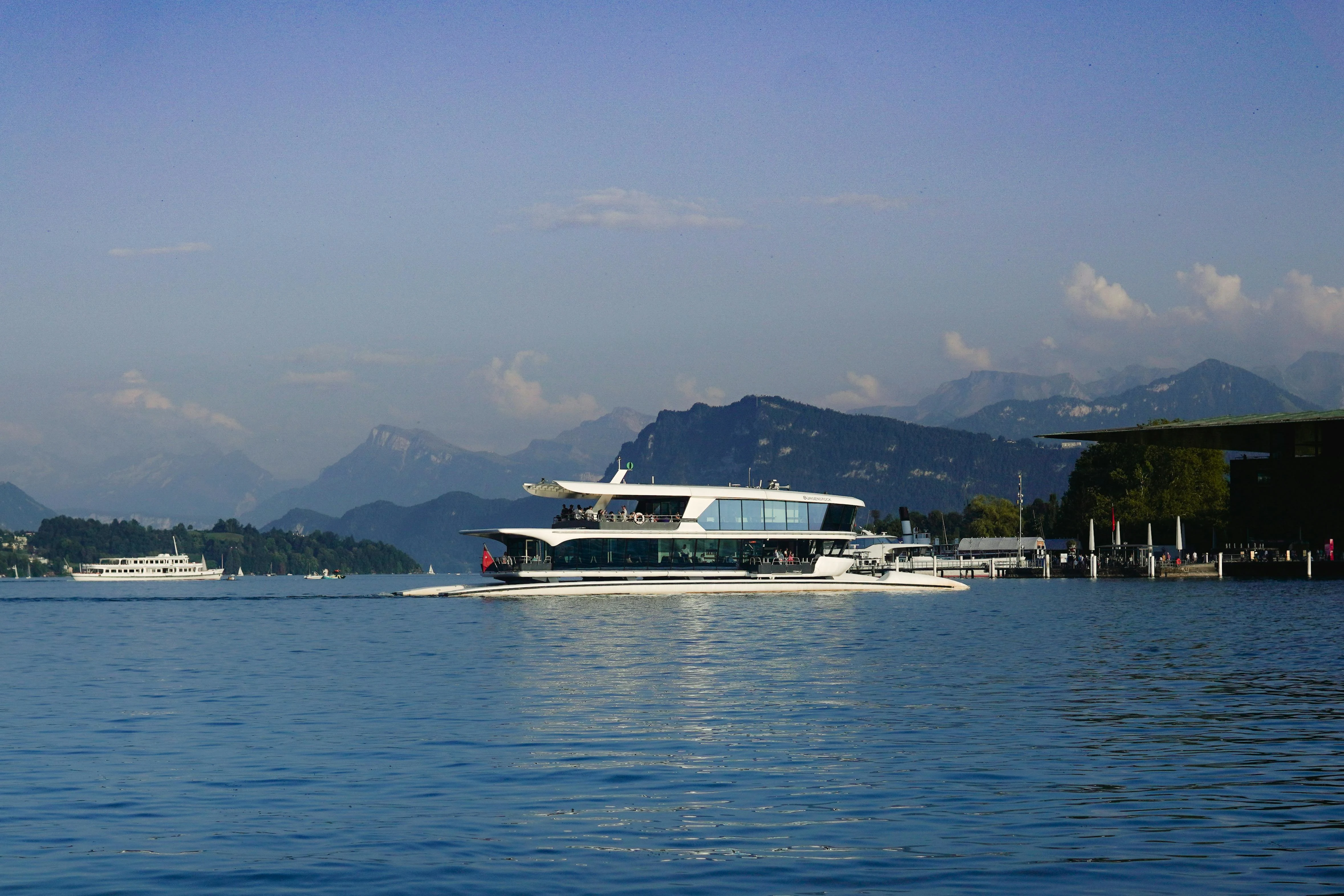 Lake Lucerne cruise boat gliding across azure waters with snow-capped Alpine peaks, historic paddle steamer, golden hour light reflecting on Vierwaldstättersee