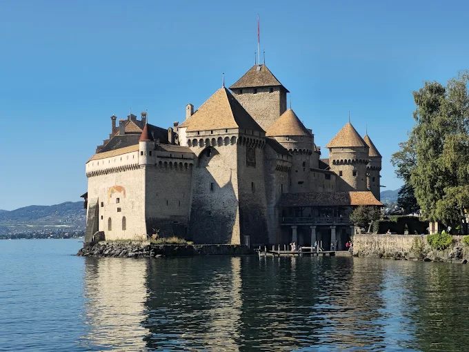 Chillon Castle medieval fortress at sunrise with Lake Geneva reflection, stone towers, and Alpine mountains in Switzerland