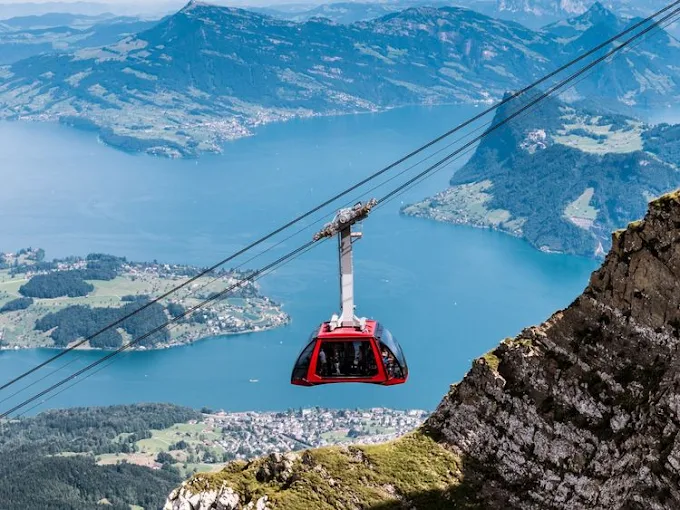 Mount Pilatus summit at sunrise with golden light hitting jagged granite peaks, Lake Lucerne below, Swiss Alps backdrop, clear blue sky