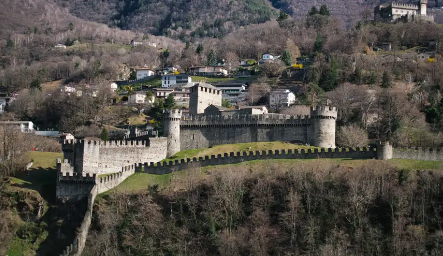 Bellinzona Castles atop rocky hills at sunset, medieval stone walls, Ticino valley below, golden hour light, UNESCO World Heritage site