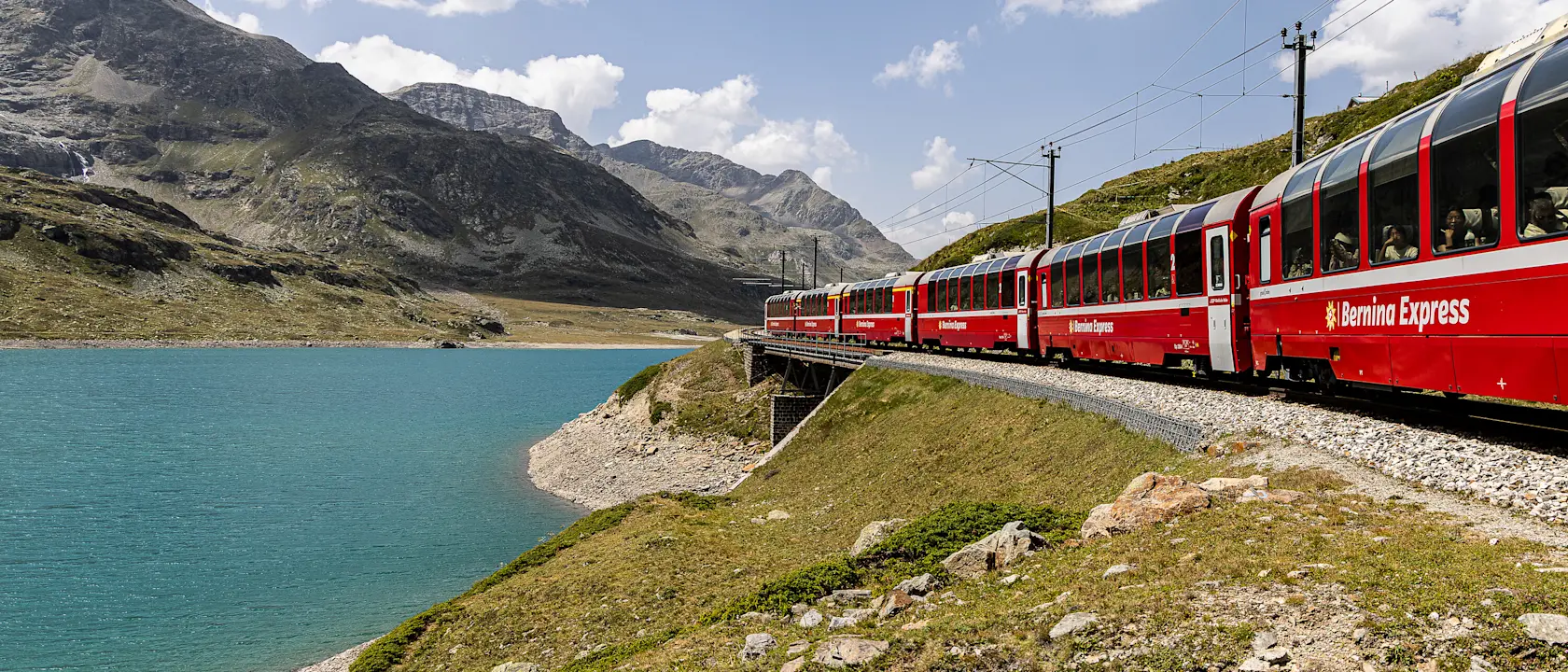 Red Bernina Express train at sunrise with panoramic windows, snowy Alps, and Brusio Viaduct in Switzerland