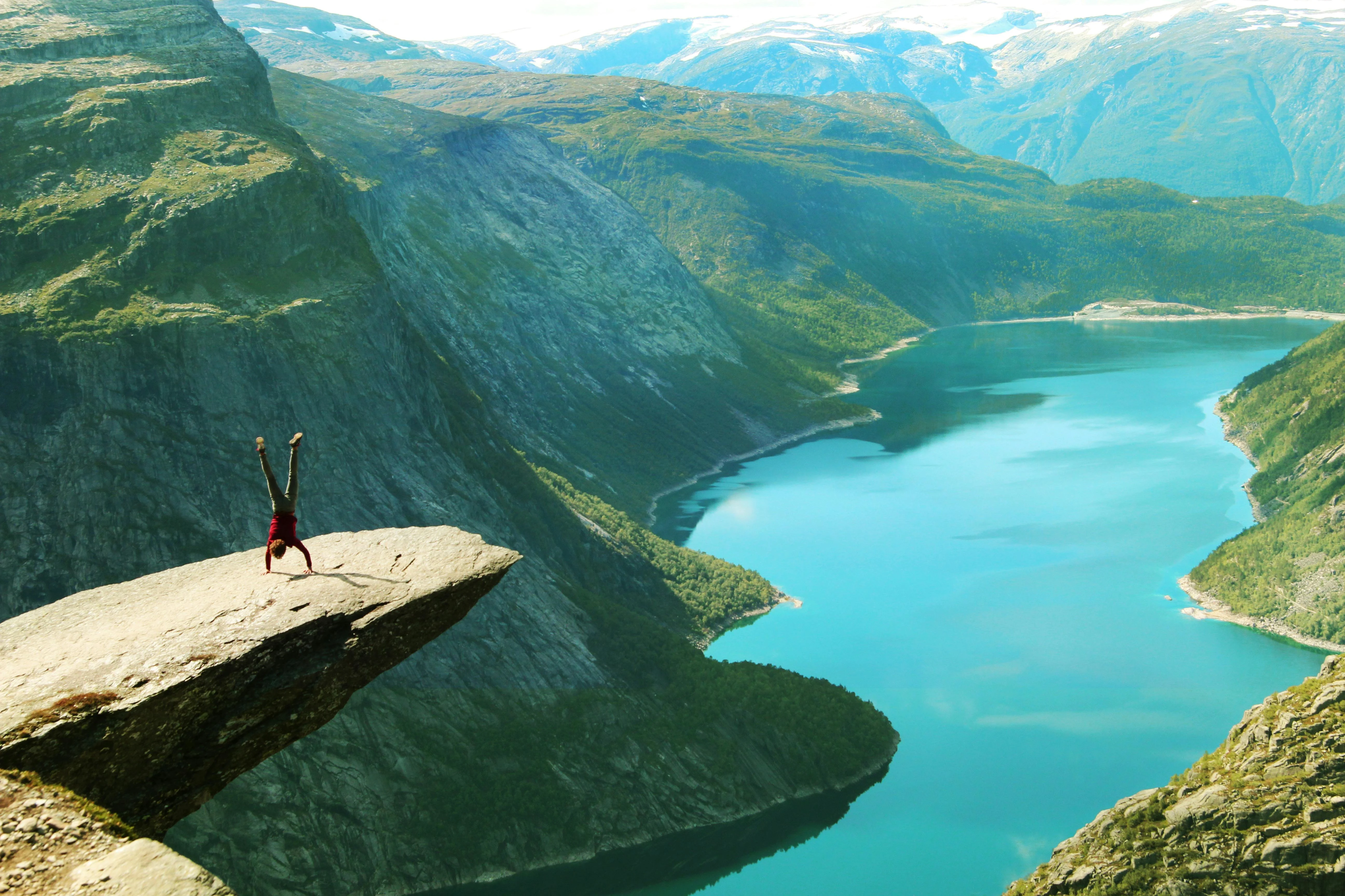 Trolltunga cliff horizontal rock formation overlooking Ringedalsvatnet lake at sunrise with hikers sitting on edge