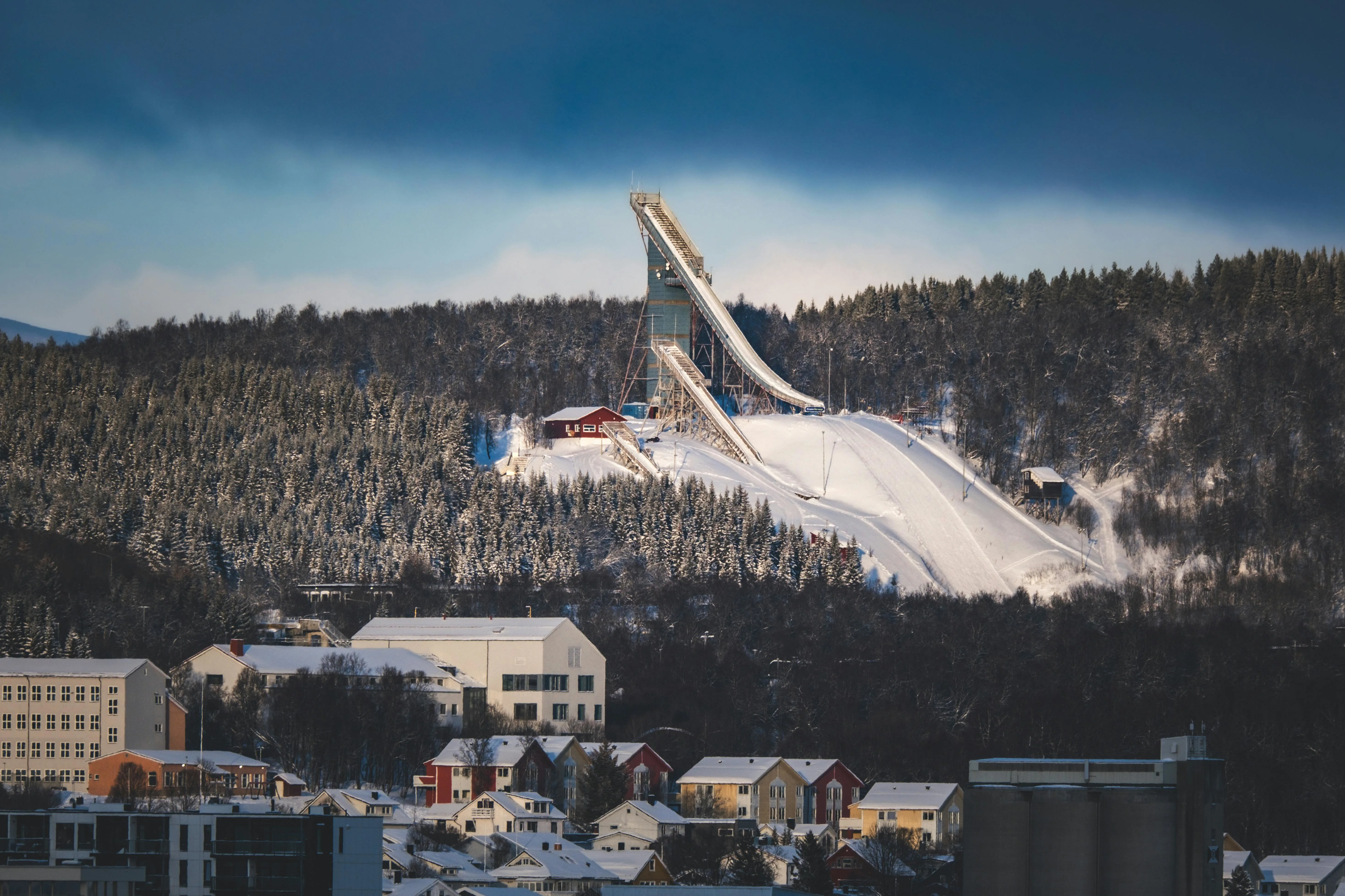 Holmenkollen Ski Jump tower against blue winter sky with Oslo cityscape and forest visible below