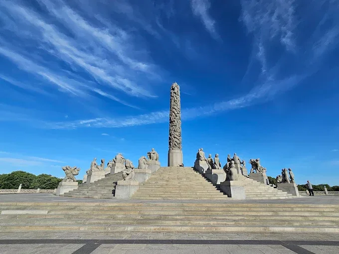 Vigeland Sculpture Park bronze Monolith sculpture at golden hour with visitors walking among statues in Oslo