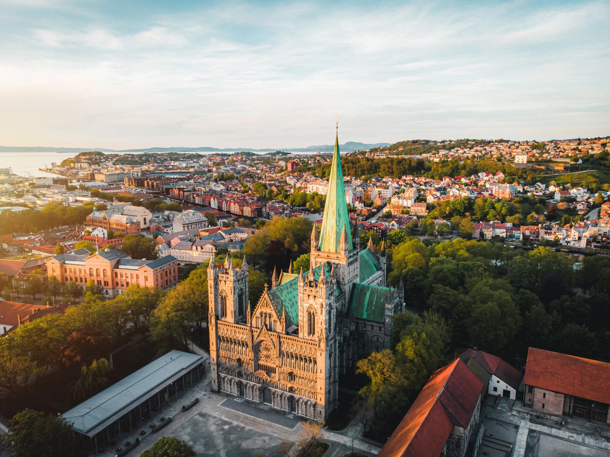 Nidaros Cathedral Gothic spires rising above Nidelva river at sunset with historic bridge and city skyline visible