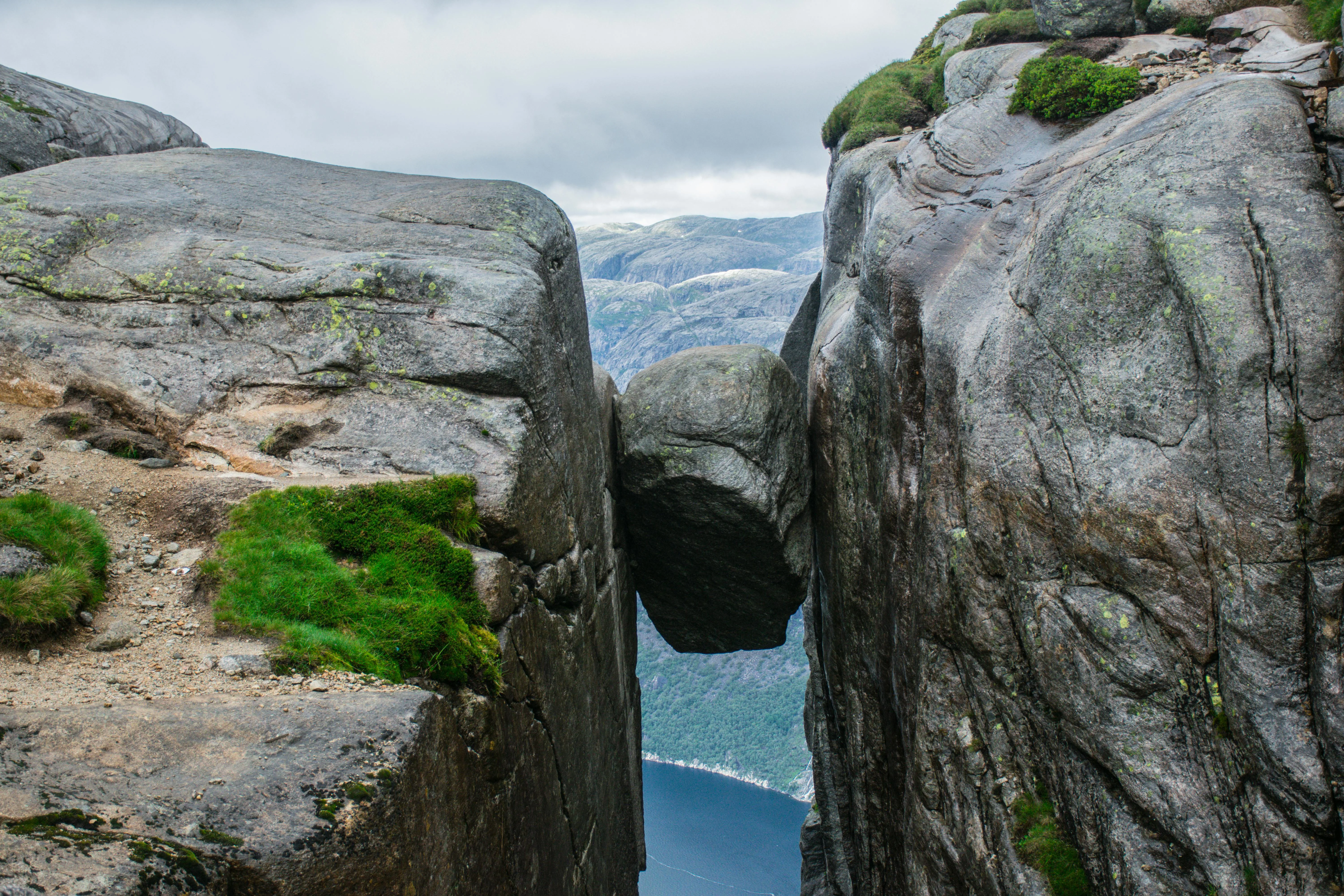 Kjeragbolten boulder wedged in mountain crevasse overlooking Lysefjord with hiker standing on stone