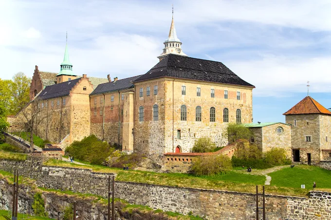 Akershus Fortress medieval stone walls overlooking Oslofjord at sunset with green lawns and historic buildings visible