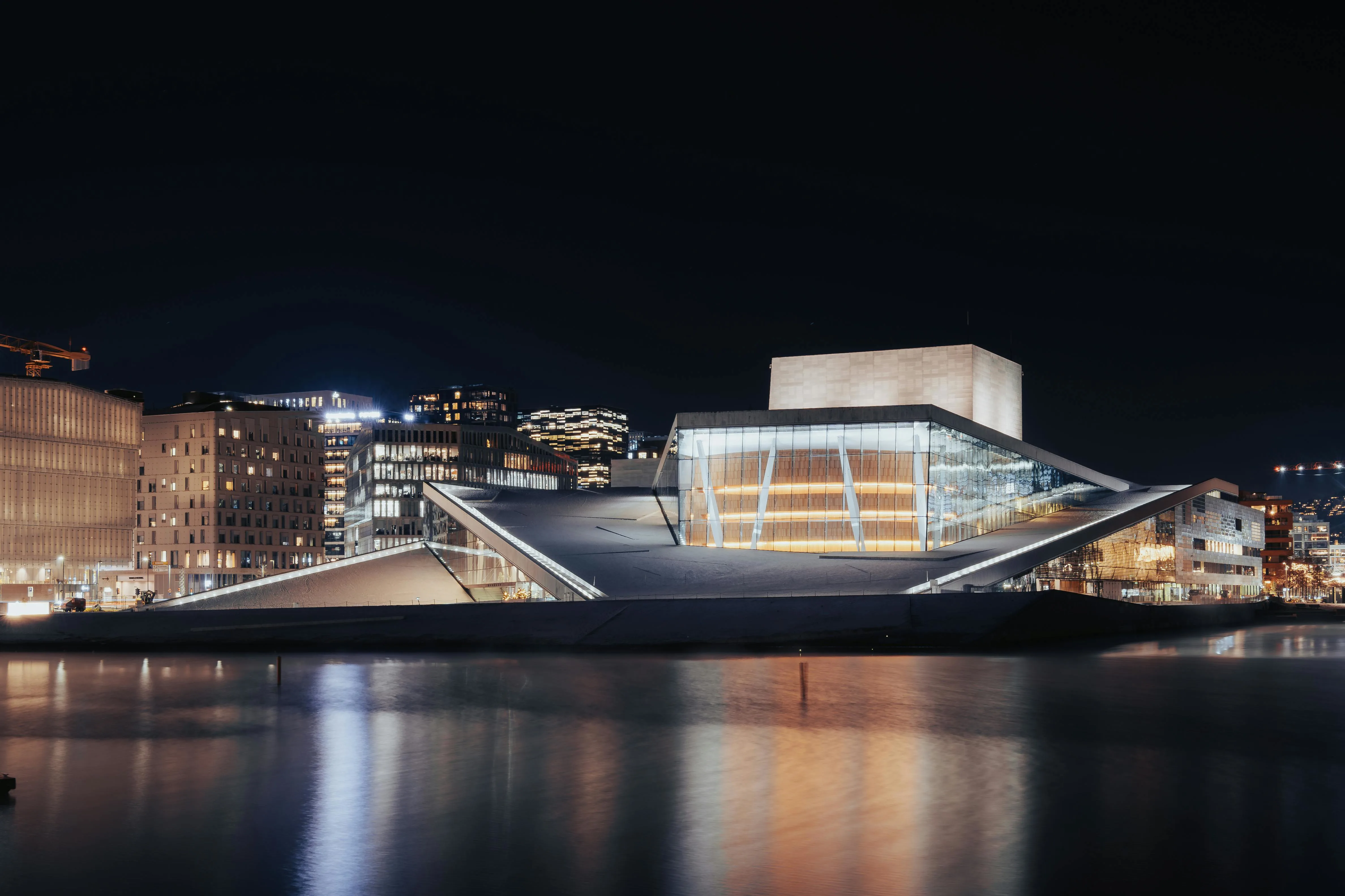 Oslo Opera House white marble roof sloping into fjord water at sunset with city skyline visible in background