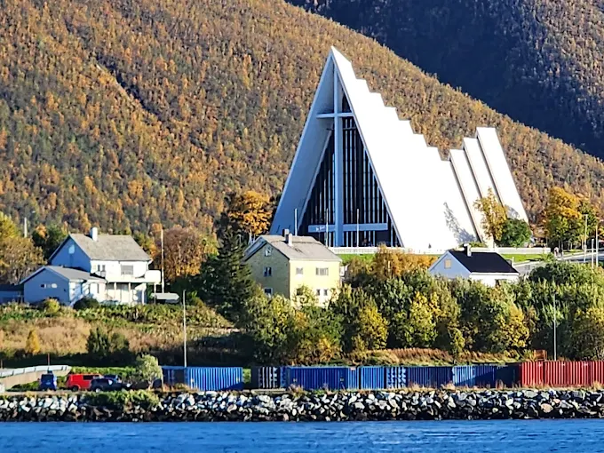 Tromsø Arctic Cathedral Norway at night with illuminated concrete triangles and northern lights dancing above snowy landscape