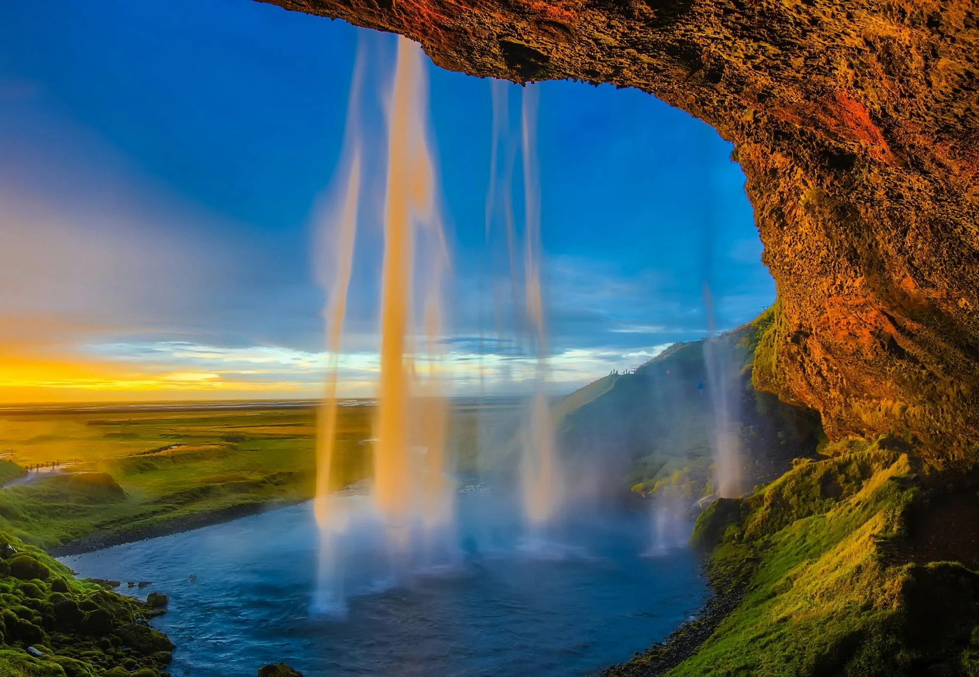 Seljalandsfoss waterfall cascading 60 meters with walk-behind path and rainbow mist at golden hour in South Iceland