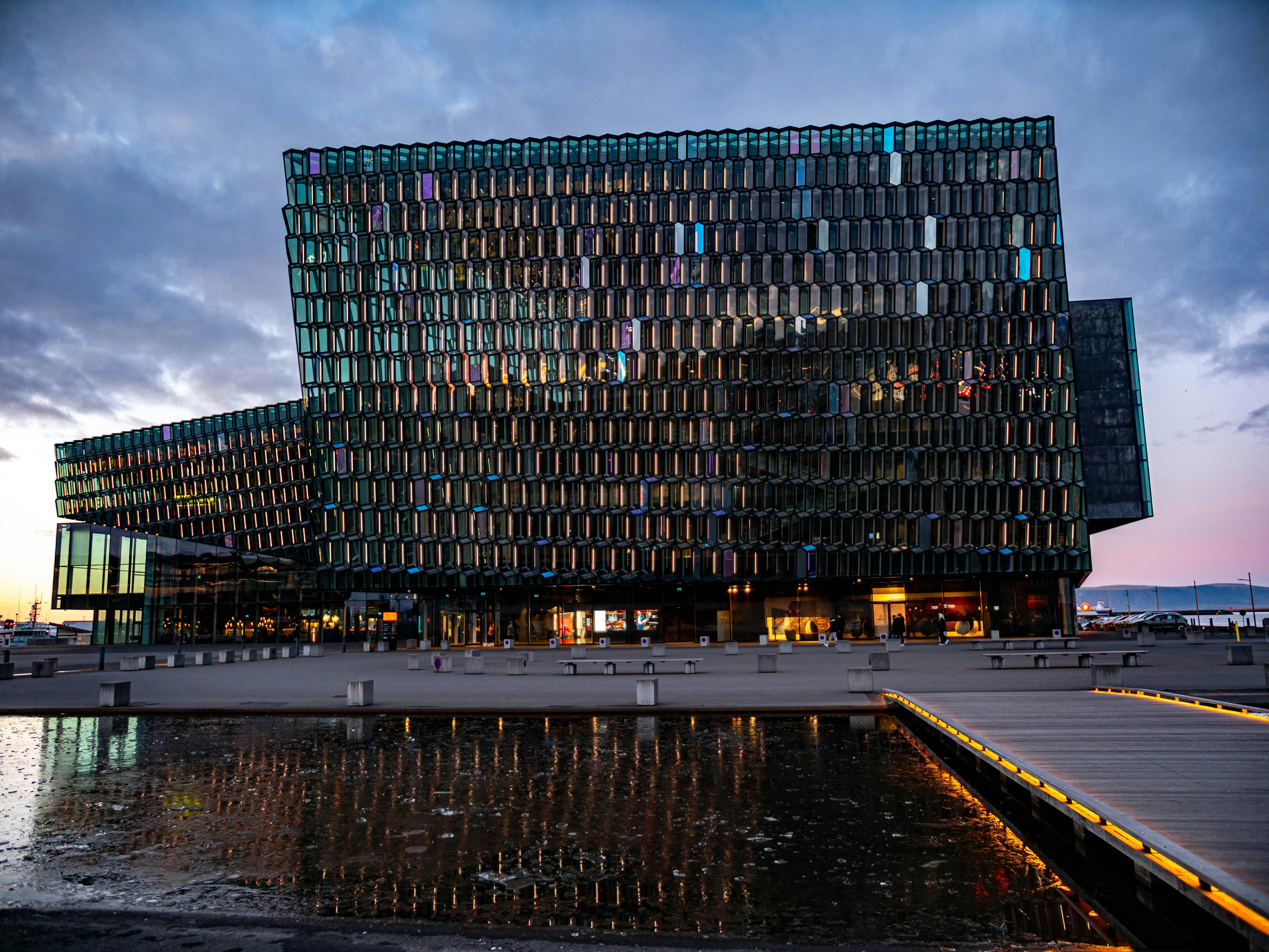 Harpa Concert Hall's honeycomb glass façade reflecting Reykjavík harbor at twilight with geometric panels glowing in Nordic blue hour light
