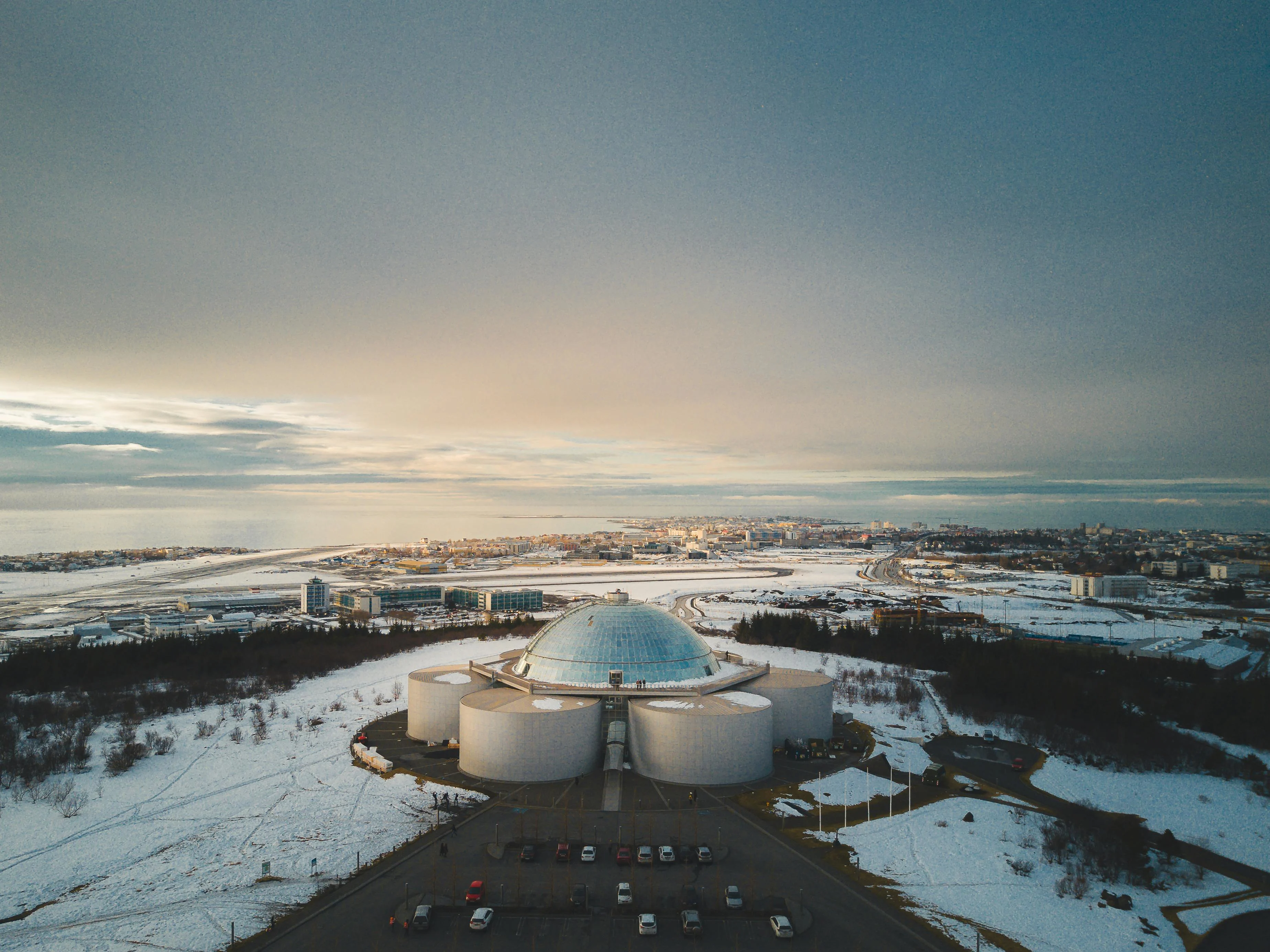 Perlan museum glass dome glowing over Reykjavík at twilight with city lights and distant mountains under Arctic sky