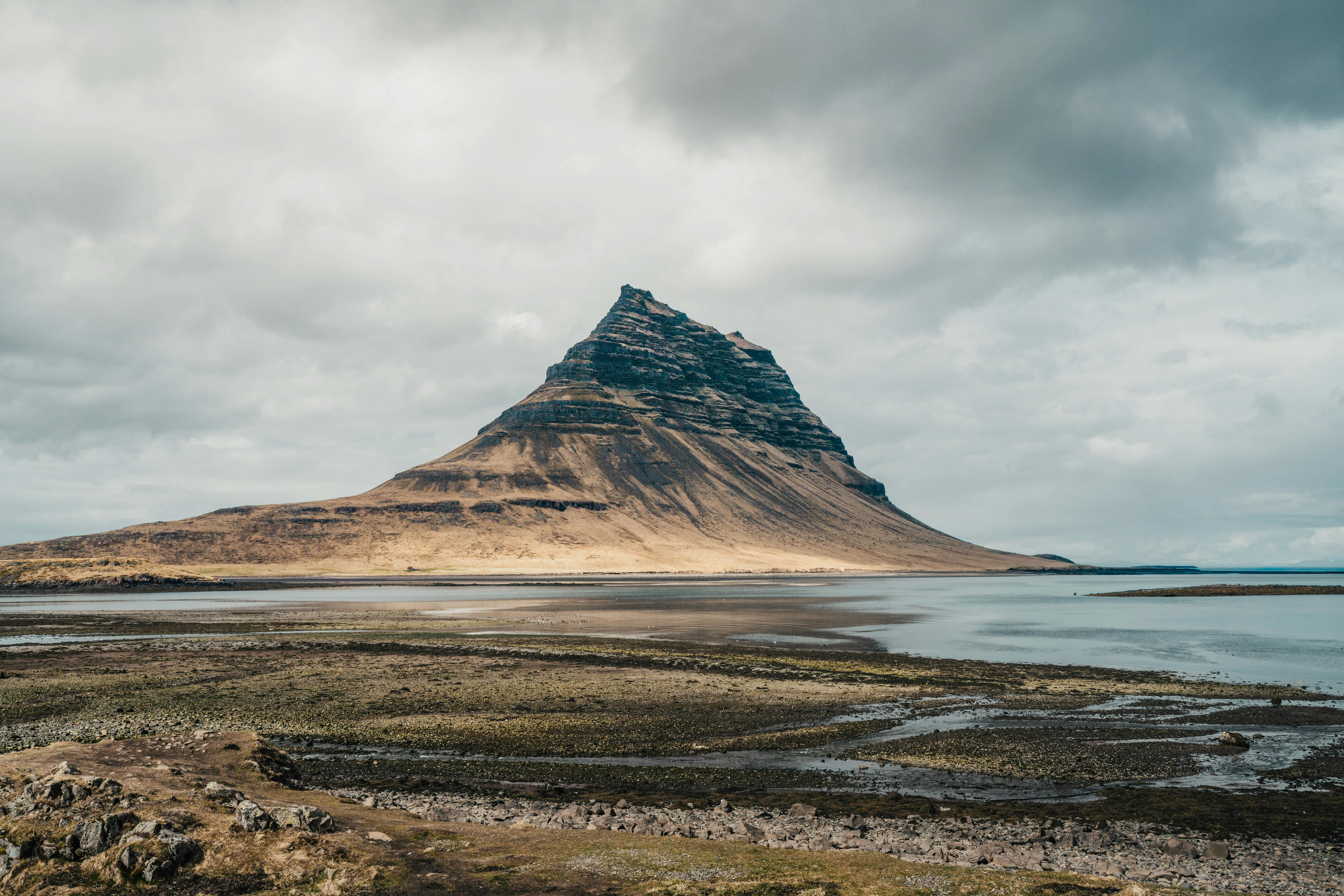 Iconic Kirkjufell mountain at sunrise in West Iceland, arrow-shaped peak reflecting in Kirkjufellsfoss waterfall foreground