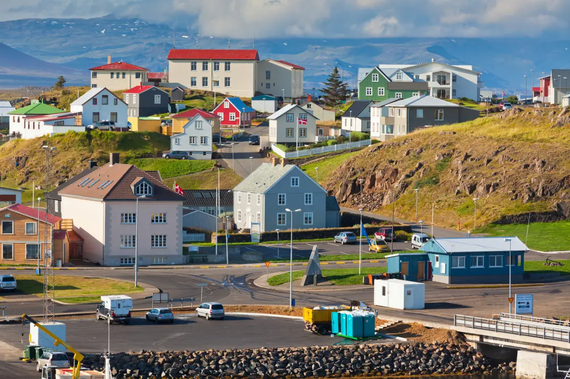 Colorful Stykkishólmur harbor at sunset in West Iceland, wooden buildings reflecting in calm water with mountains backdrop