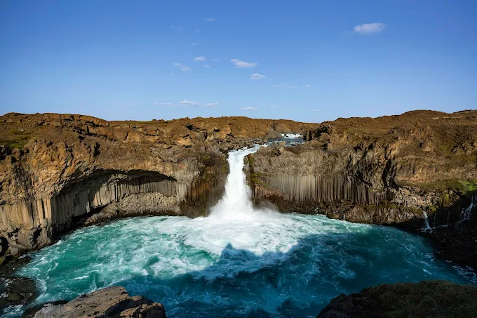 Aldeyjarfoss waterfall cascading over black basalt columns in North Iceland summer sunlight with turquoise river below