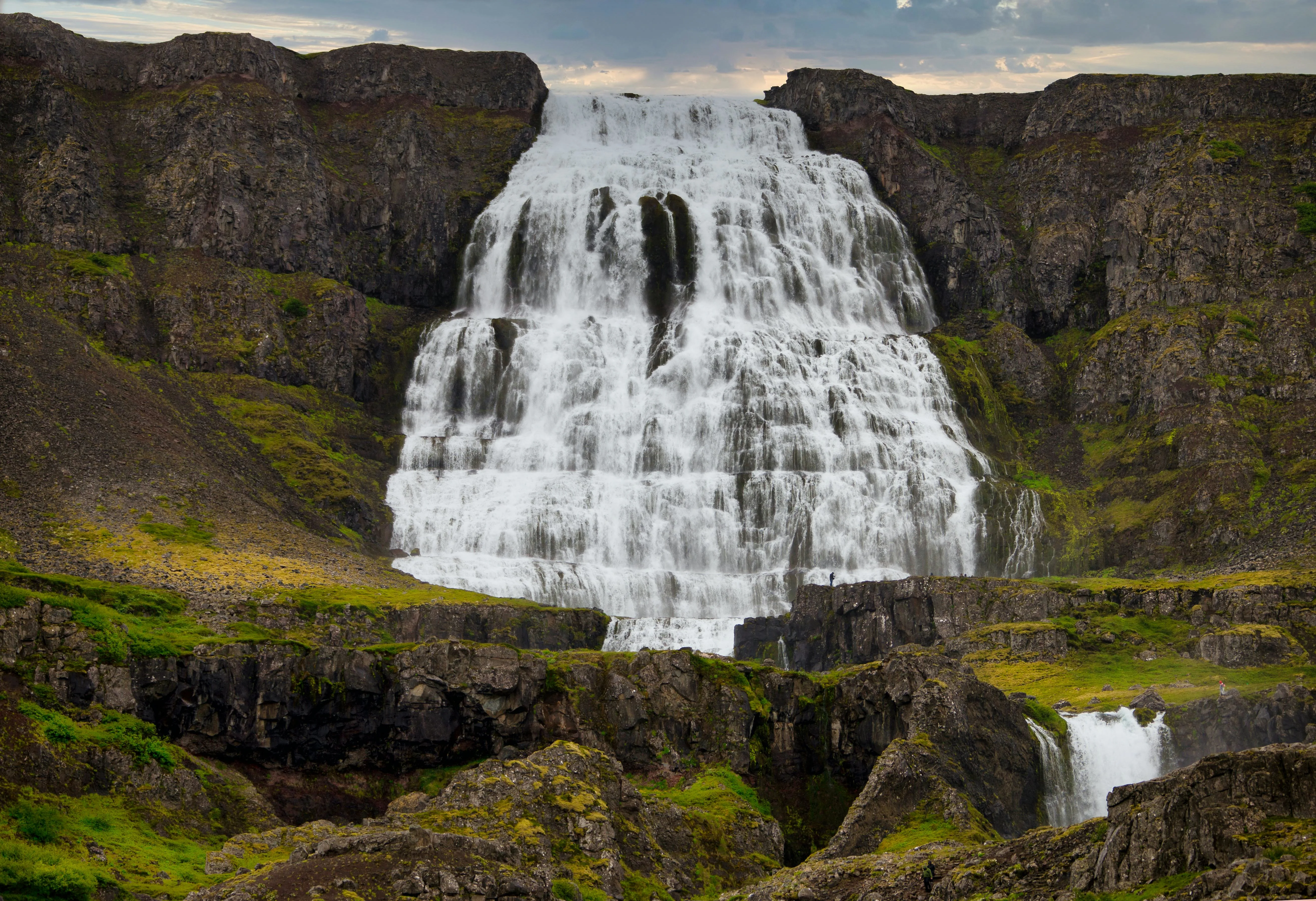 Dynjandi waterfall cascading down Westfjords cliff face at golden hour with mist rising from multiple tiers