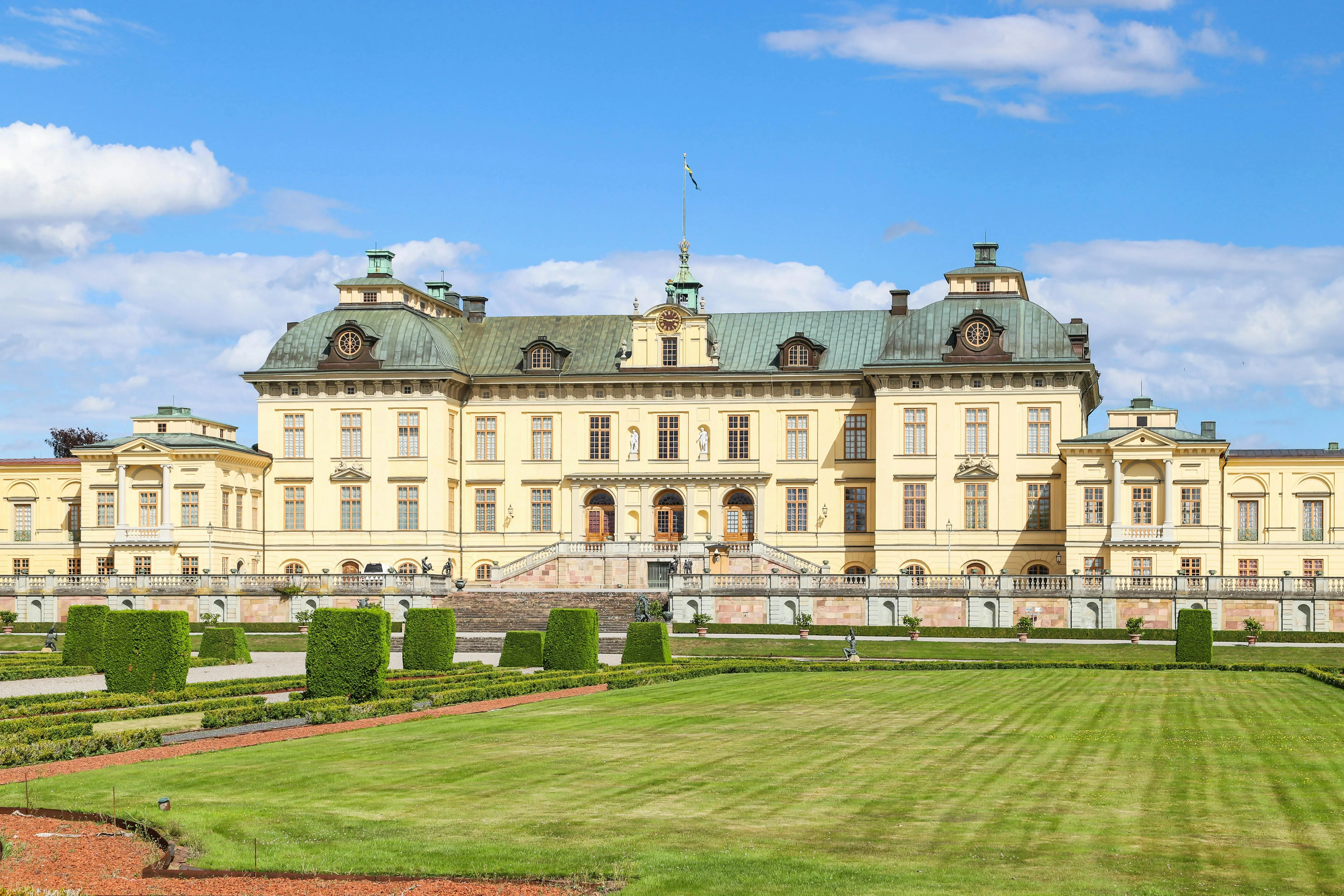 Drottningholm Palace yellow facade reflecting in canal at golden hour with formal gardens in foreground